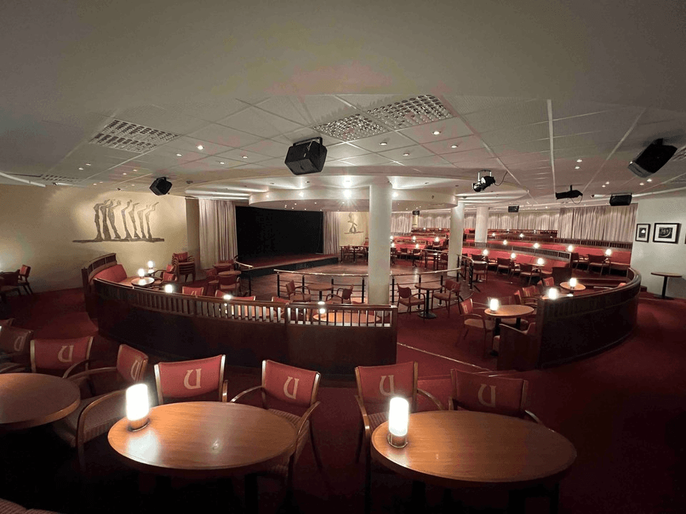 A cozy indoor venue with small tables and chairs, softly lit, creating an intimate atmosphere.