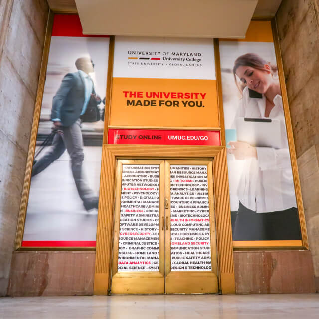 Entrance with signs for University of Maryland Global Campus, featuring slogans and images of a business professional and a woman on the phone—highlighting creative media often used by an advertising agency Baltimore relies on for strong brand strategy.