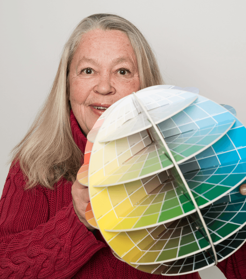 Smiling woman holds a patented 3D color globe displaying hue, value and chroma for hands-on color education.