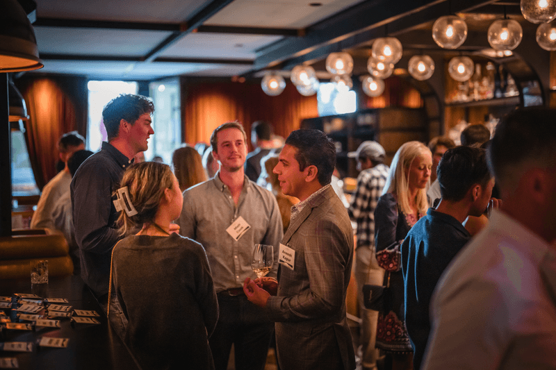 Attendees wearing name badges talking over drinks beneath globe pendant lights