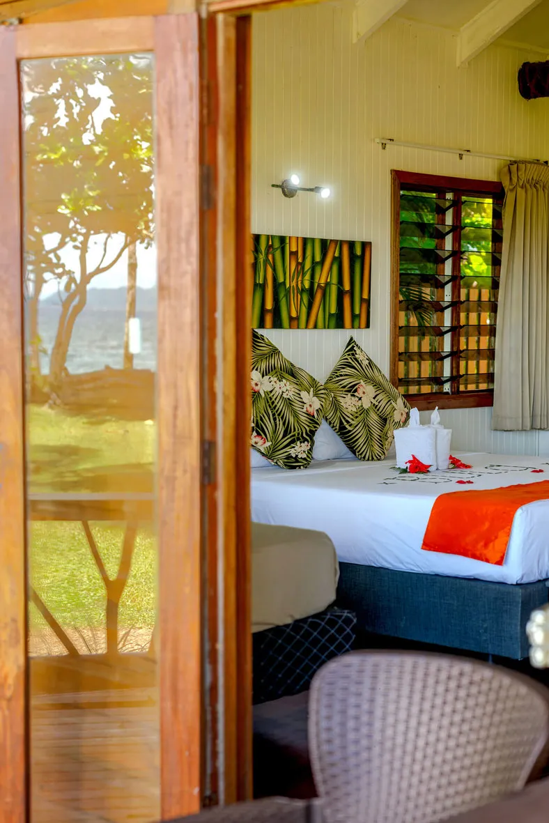 Bure at Uprising Beach Resort Fiji with a reflection of the beach in the glass and revealing the bed and tasteful decor