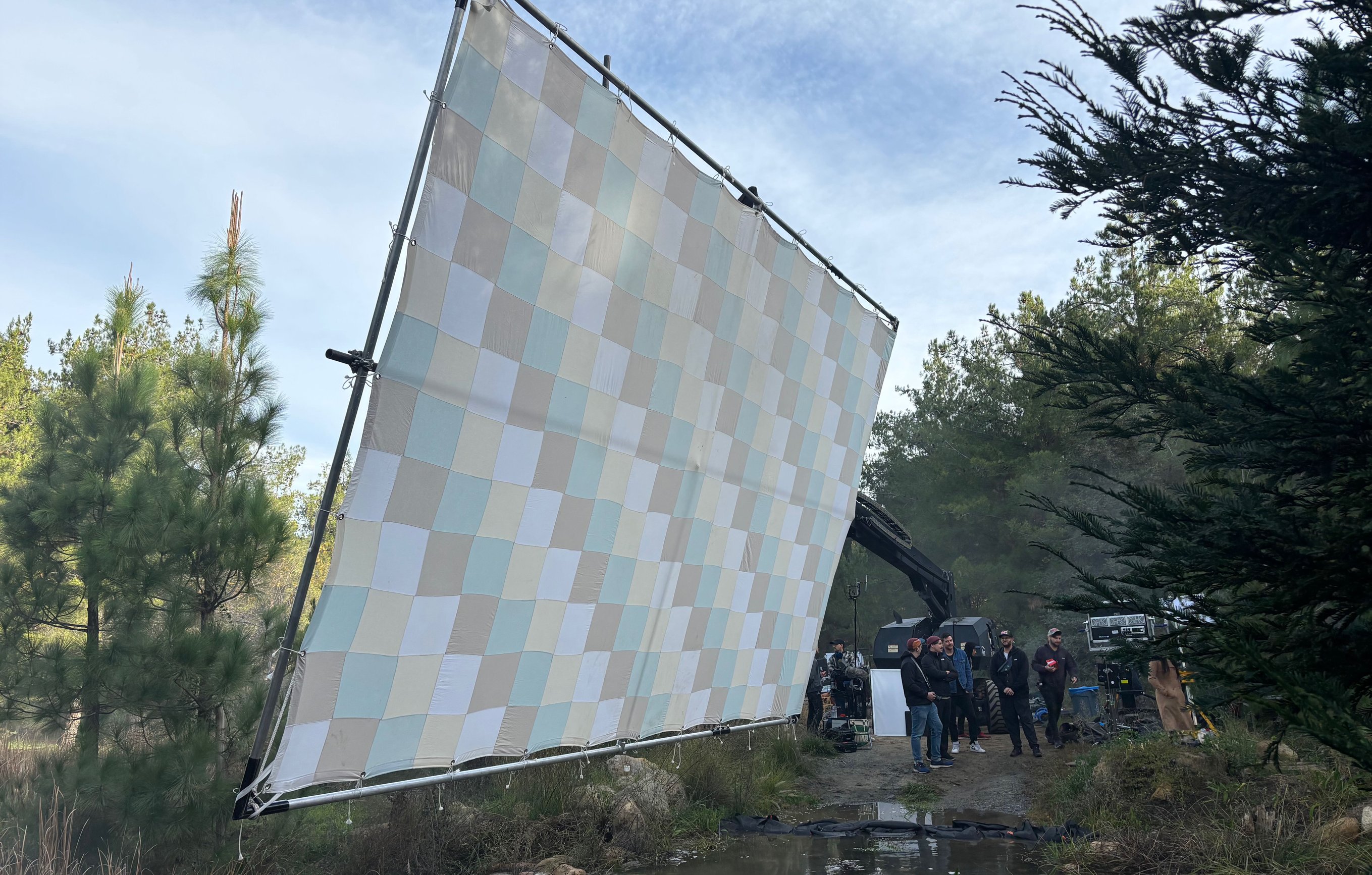 12x20 checker bounce tilted nearly vertical near the loading position, side profile of the speedrail frame, crew gathered in the background by the Condor, creek visible at lower right.