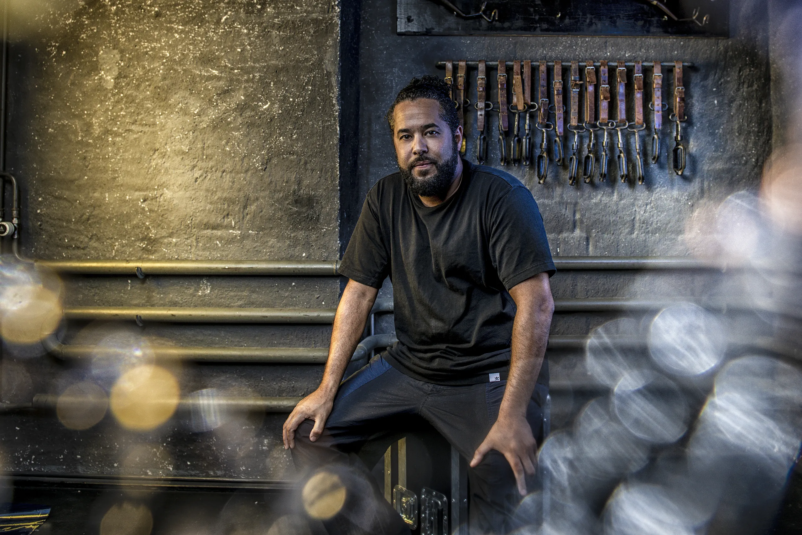 Atmospheric portrait of Adel Tawil sitting in a dimly lit backstage area with warm bokeh lights.