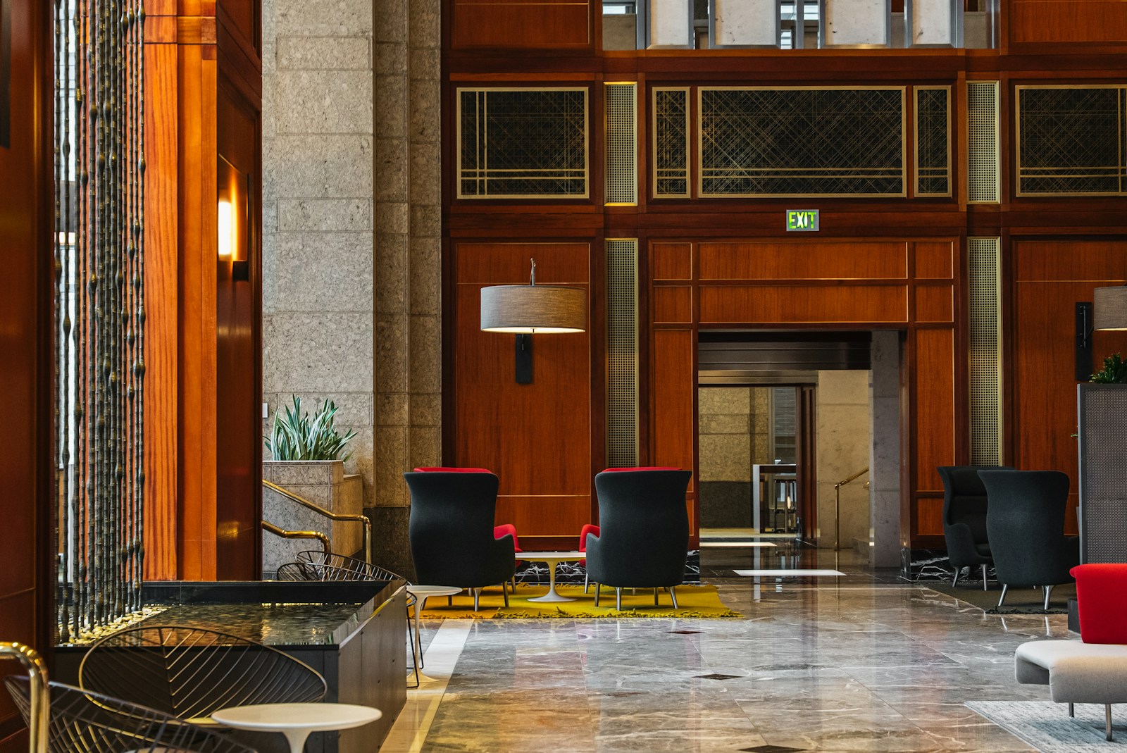Hotel lobby with tall stone columns, warm wood paneling, polished tile flooring, and grouped lounge seating.