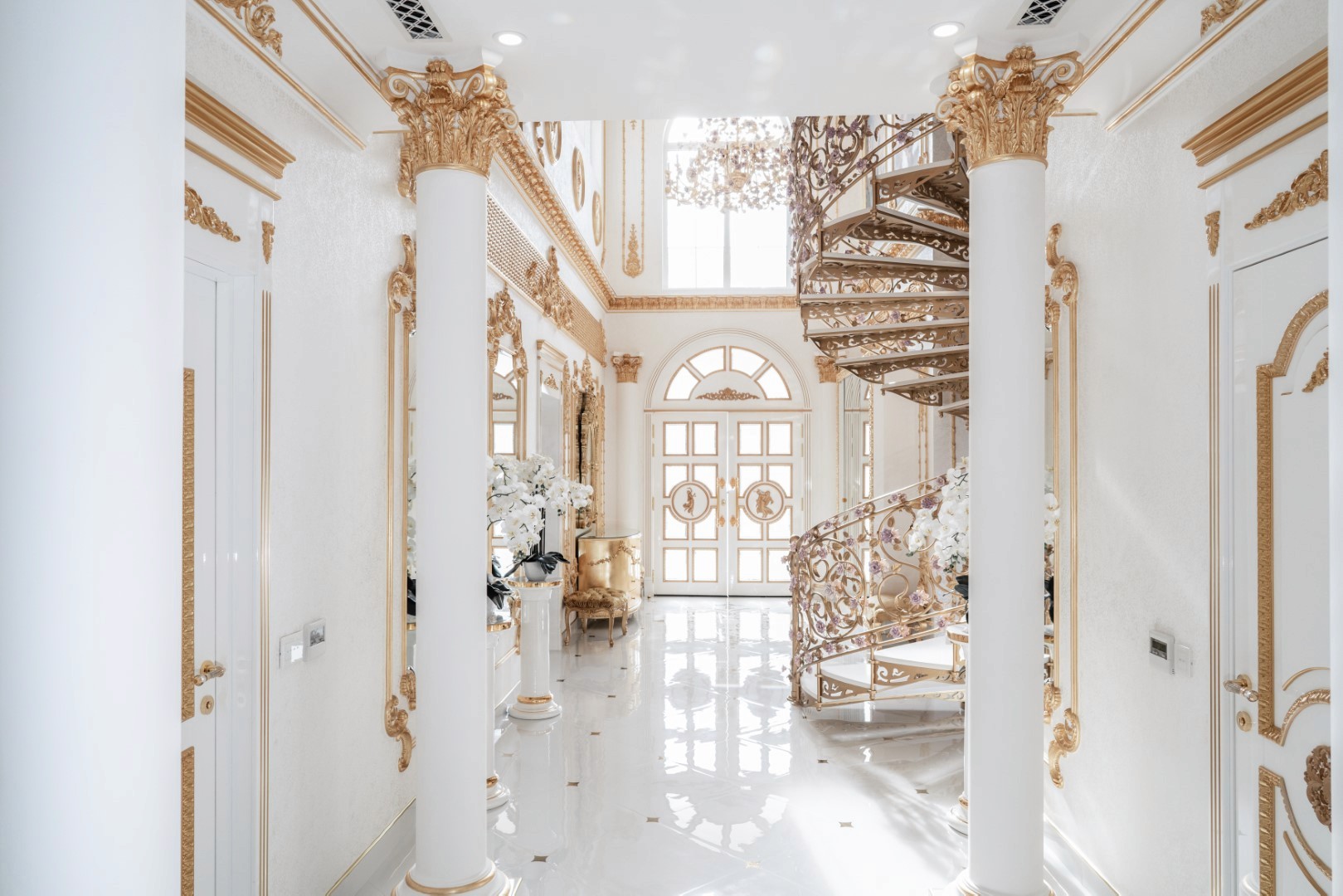 Luxurious interior hallway featuring ornate gold and white decor, with a grand spiral staircase, towering columns, opulent chandeliers, and intricate wall detailing, exemplifying classic elegance and sophistication.