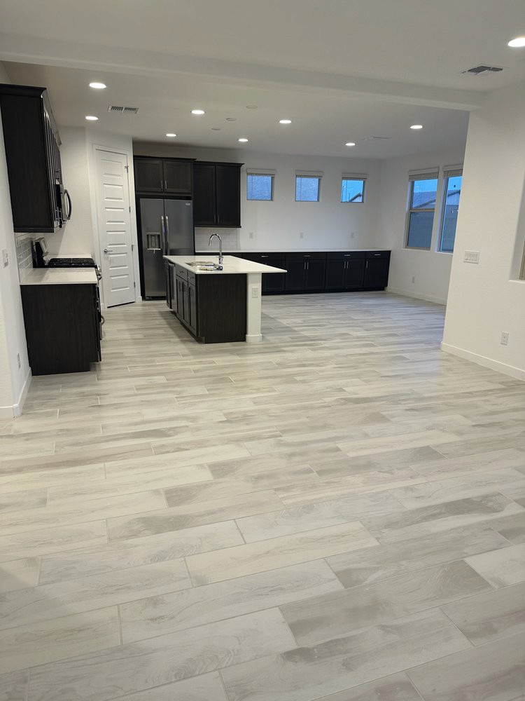 Modern kitchen with dark cabinets, stainless steel appliances, white countertops, and wood-look tiles.