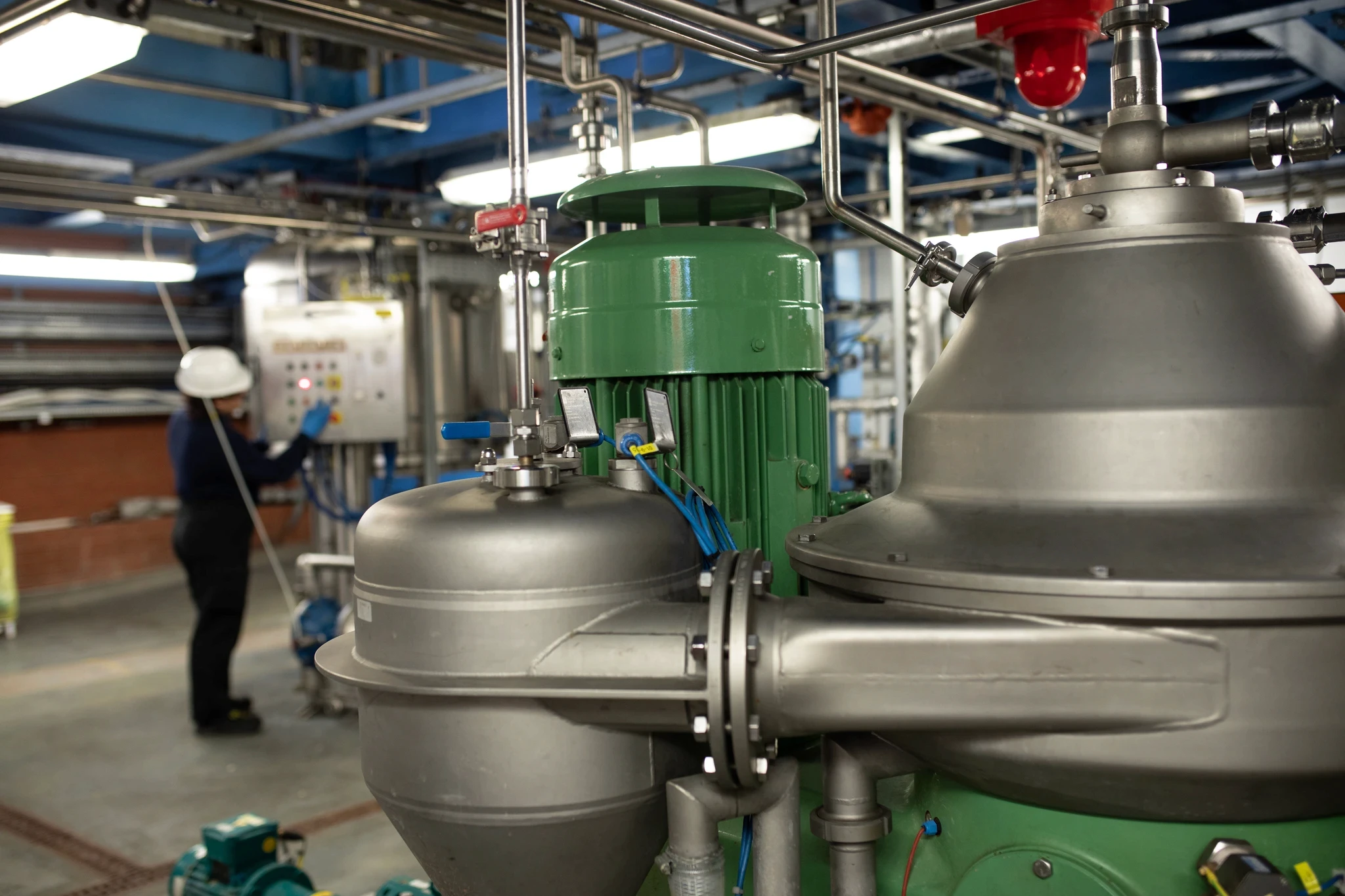 Stainless steel disc-stack centrifuge with a green motor, with an operator working in the background.