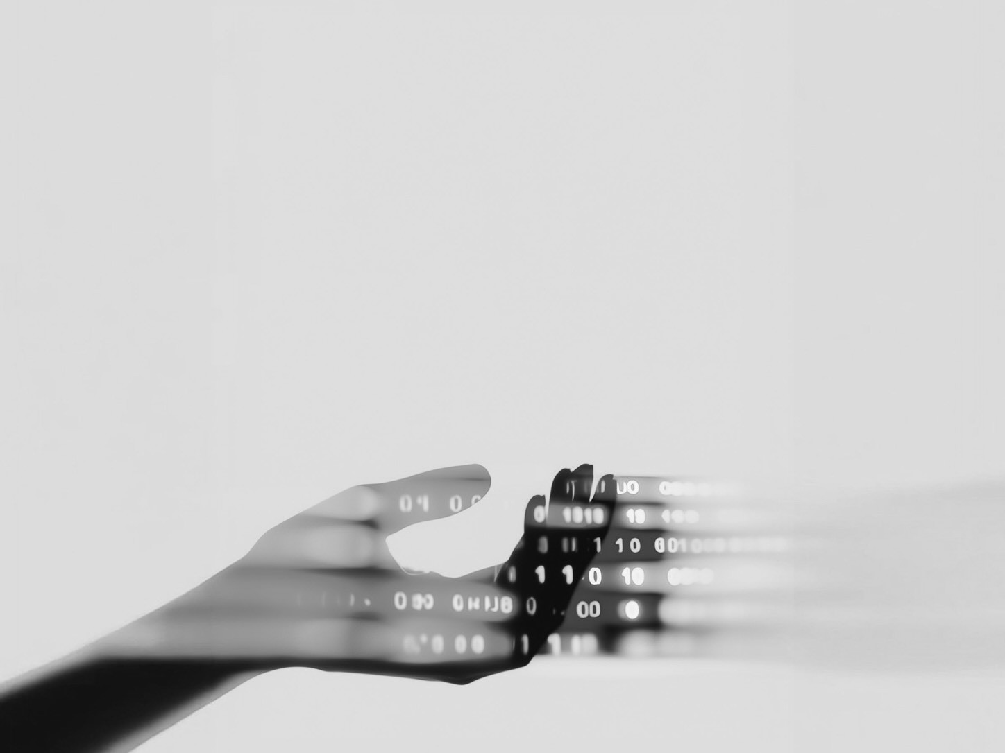 Black-and-white conceptual image of a hand holding a stack of digital code, with glowing binary-like characters streaming across the fingers.