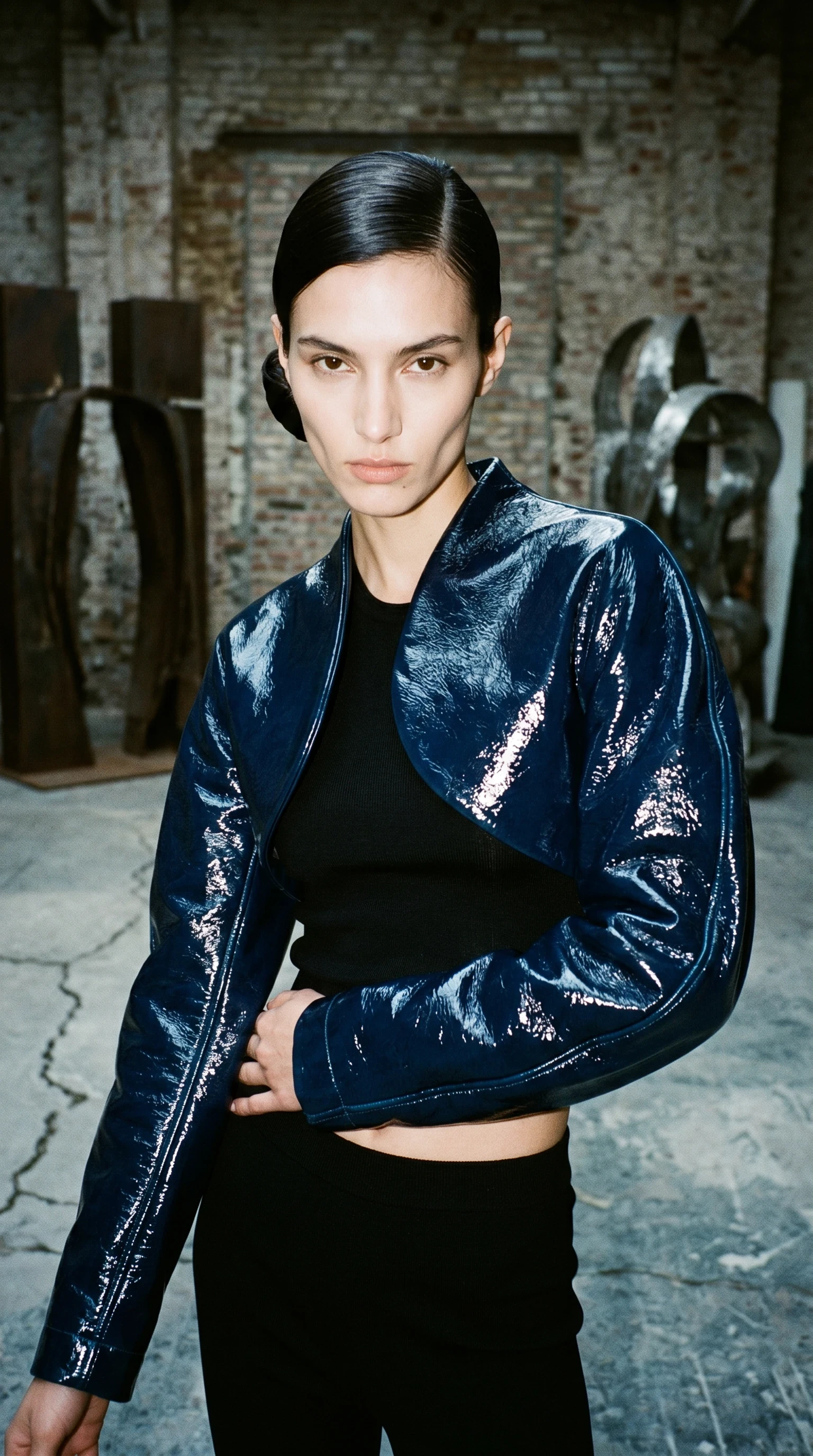 Female model wearing dark blue patent cocoon bolero facing the camera.
