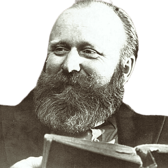 This is a black-and-white portrait of a bearded man with a warm smile, wearing a suit and holding an open book. His full beard and expressive face give him a distinguished, scholarly appearance, suggesting a historical figure, possibly a writer, philosopher, or intellectual from the late 19th or early 20th century.