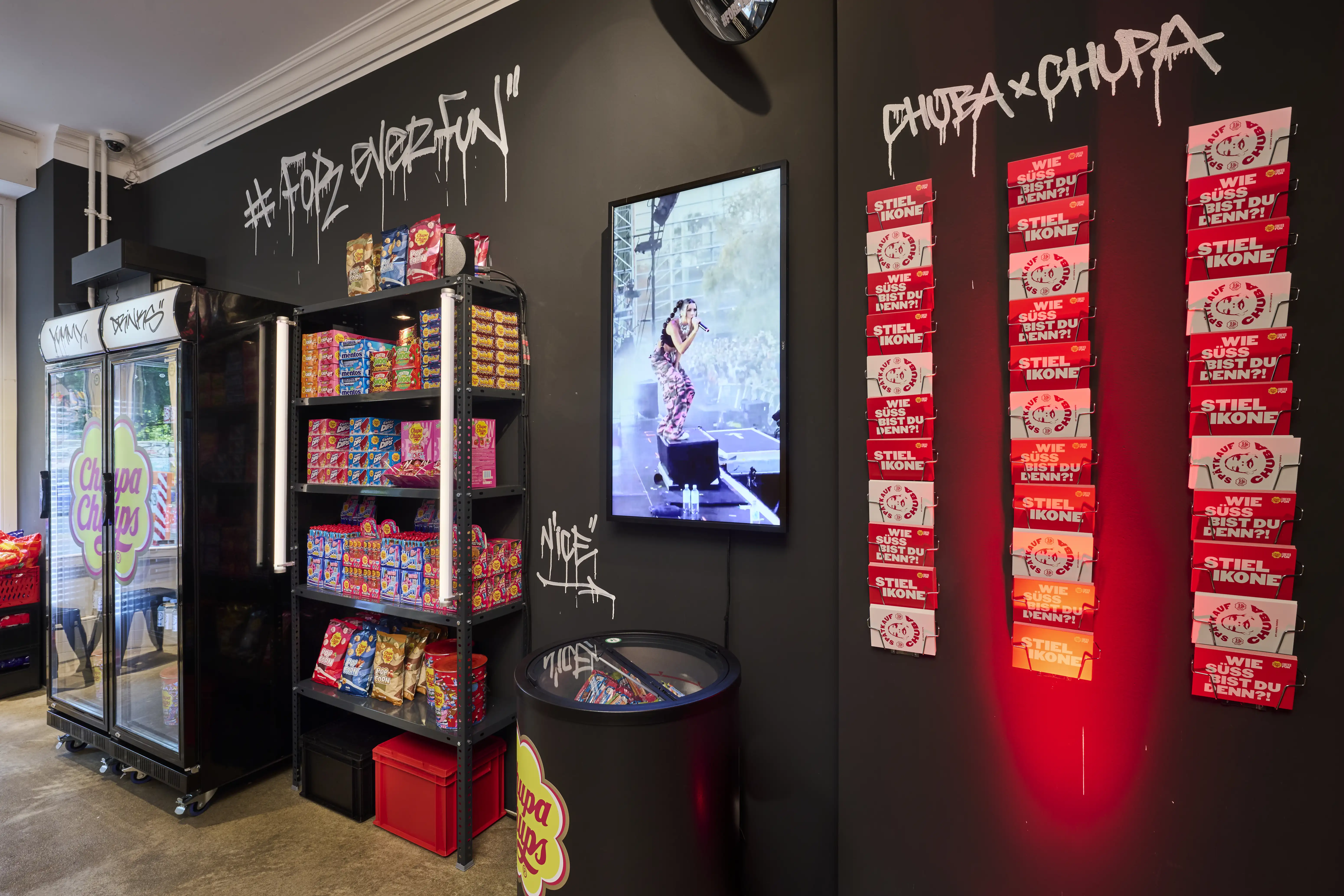 Screen with concert footage and red Chuba x Chupa card wall next to candy shelves in the pop-up kiosk.