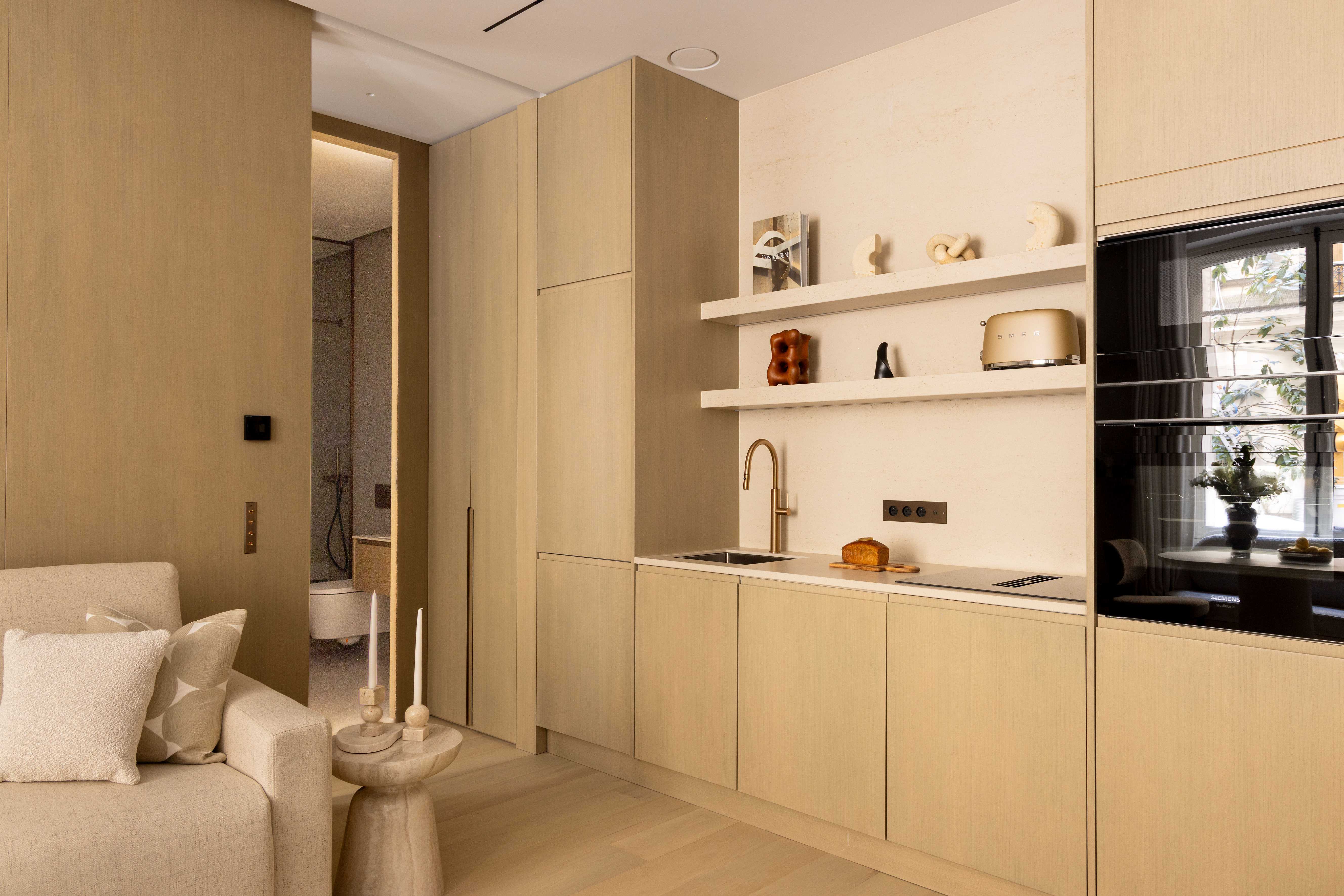 Cuisine équipée intégrée en bois clair avec évier, étagères décoratives et four encastré noir