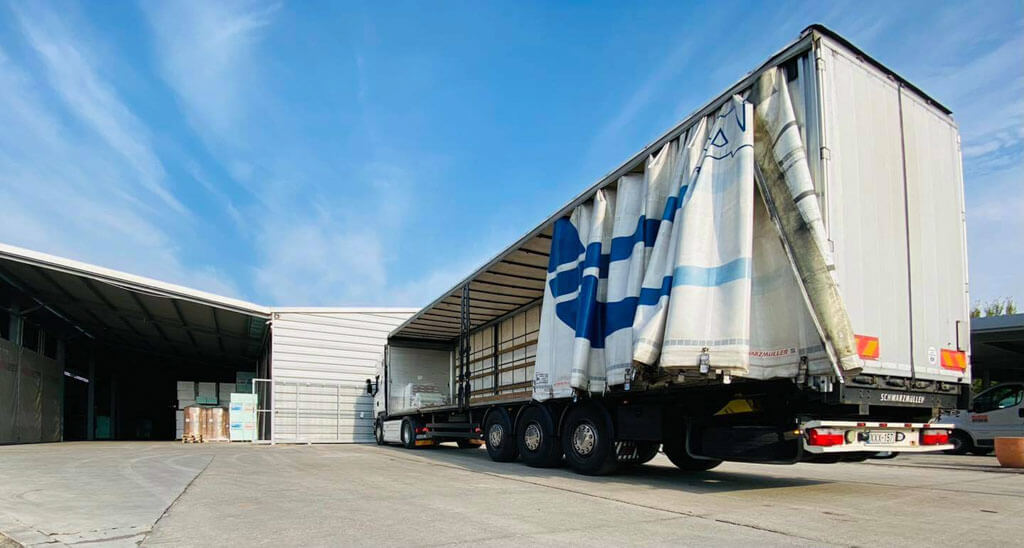 Áruszállításra, fuvarozásra alkalmas ponyvás nyerges kamion egy rakodási területen