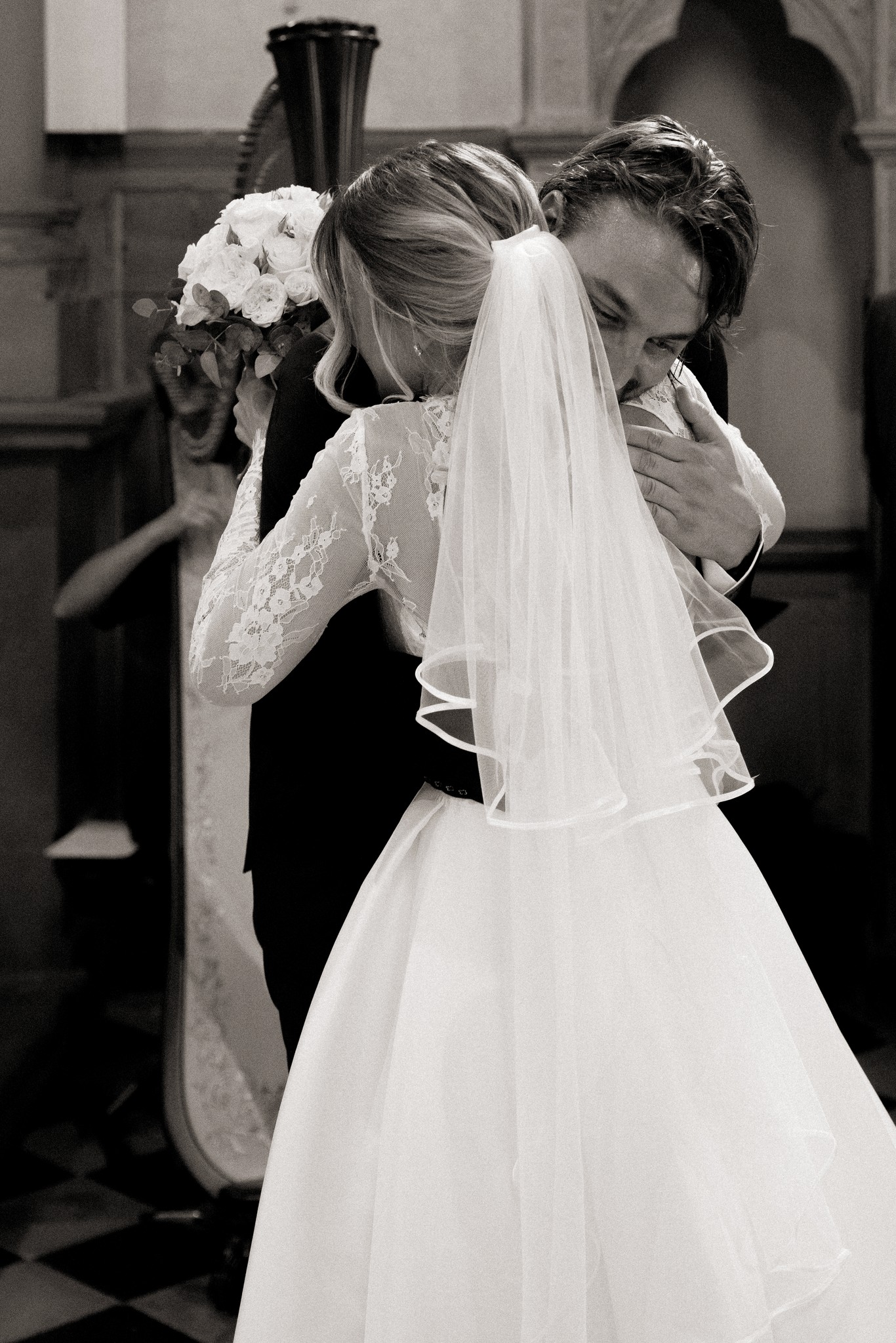 Sposo bacia la sposa sotto il velo in chiesa a Bolgheri, primo momento di matrimonio in bianco e nero
