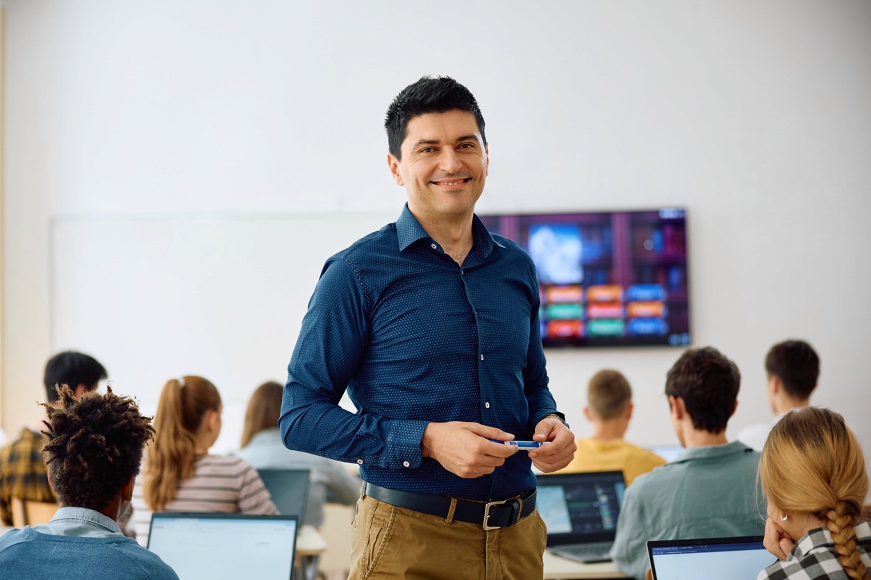 Teacher smiling in front of a class of students with a display screen behind them