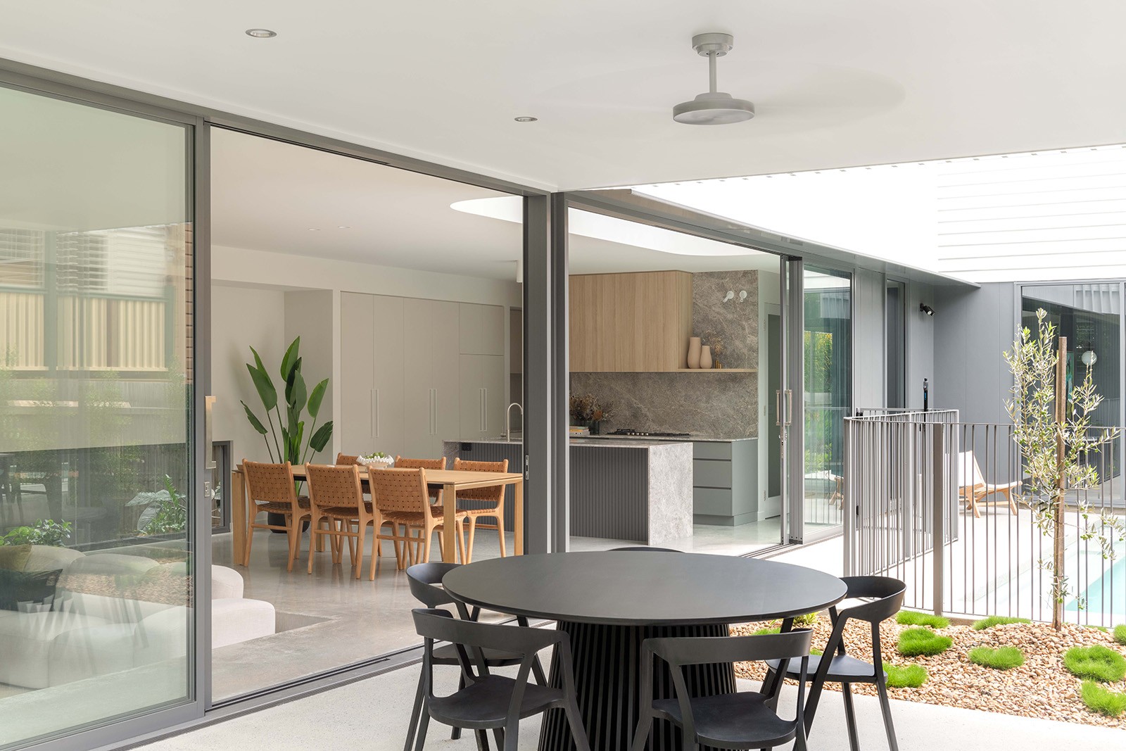 Courtyard-facing dining space at The Stables, where sliding glass doors dissolve the boundary between indoor living and the landscaped outdoor zone.