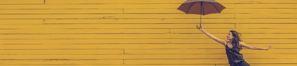Woman dancing with umbrella against yellow wall background