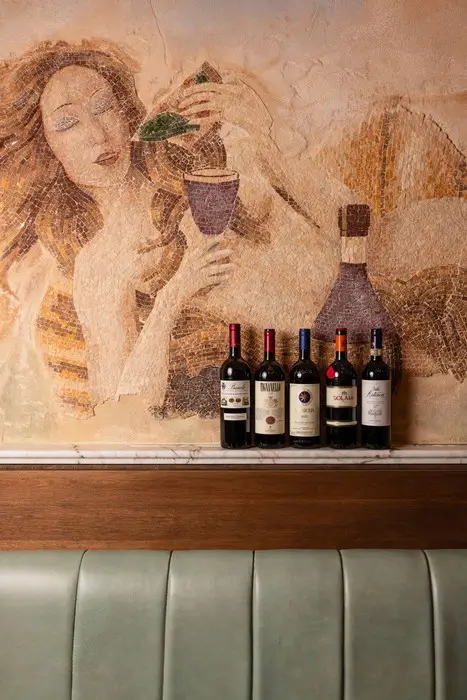 Photo d'une sélection de vins italiens de choix, installé devant la mosaïque murale signature du restaurant Bartolino, avec sa Vénus et son Vésuve