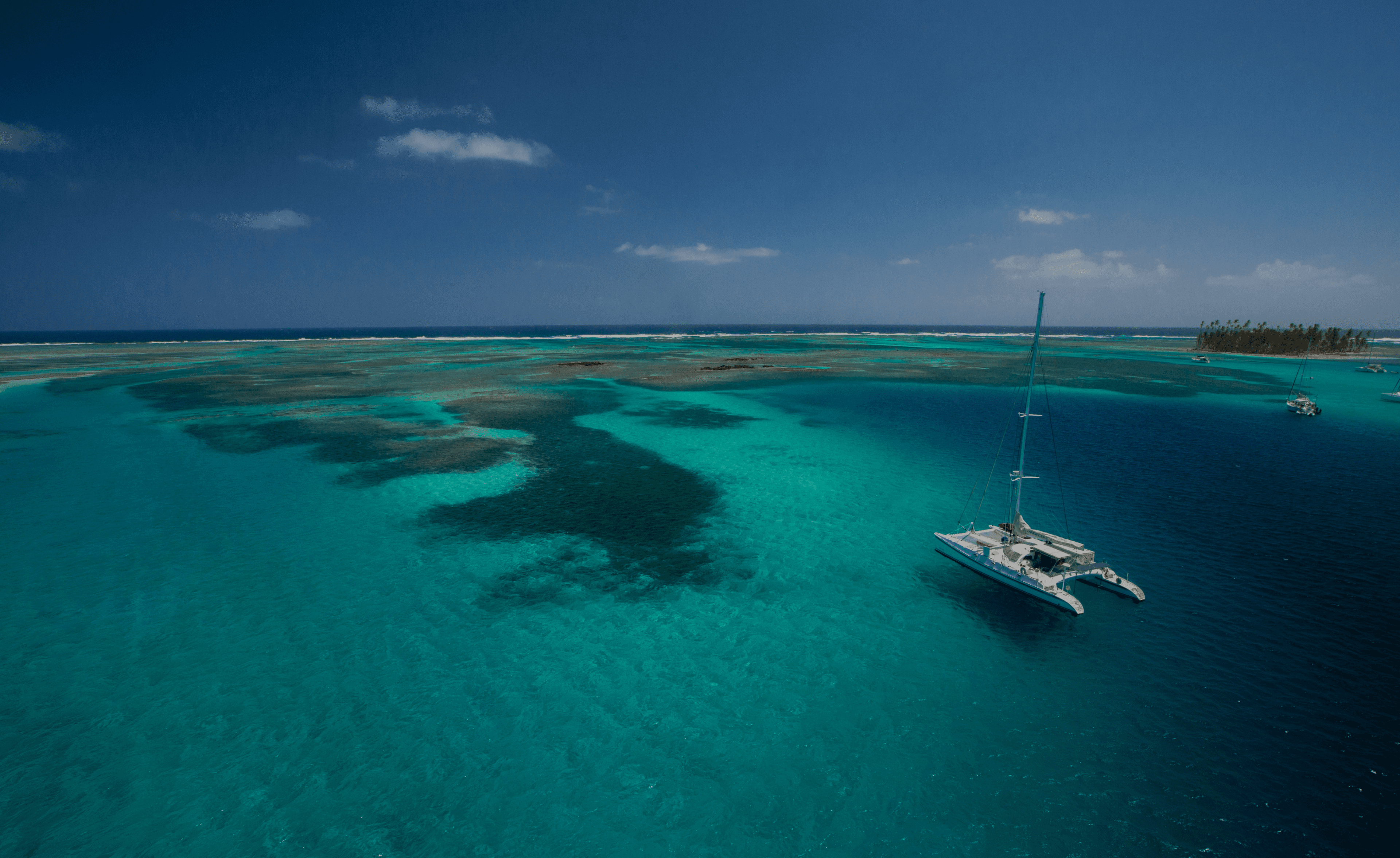 Catamaran anchored in turquoise tropical water near coral reefs and island.