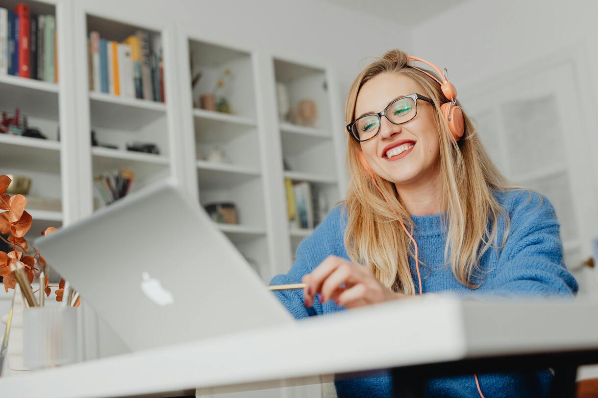 A lady in her home, smiling at her laptop while providing web design services and wearing cream coloured headphones