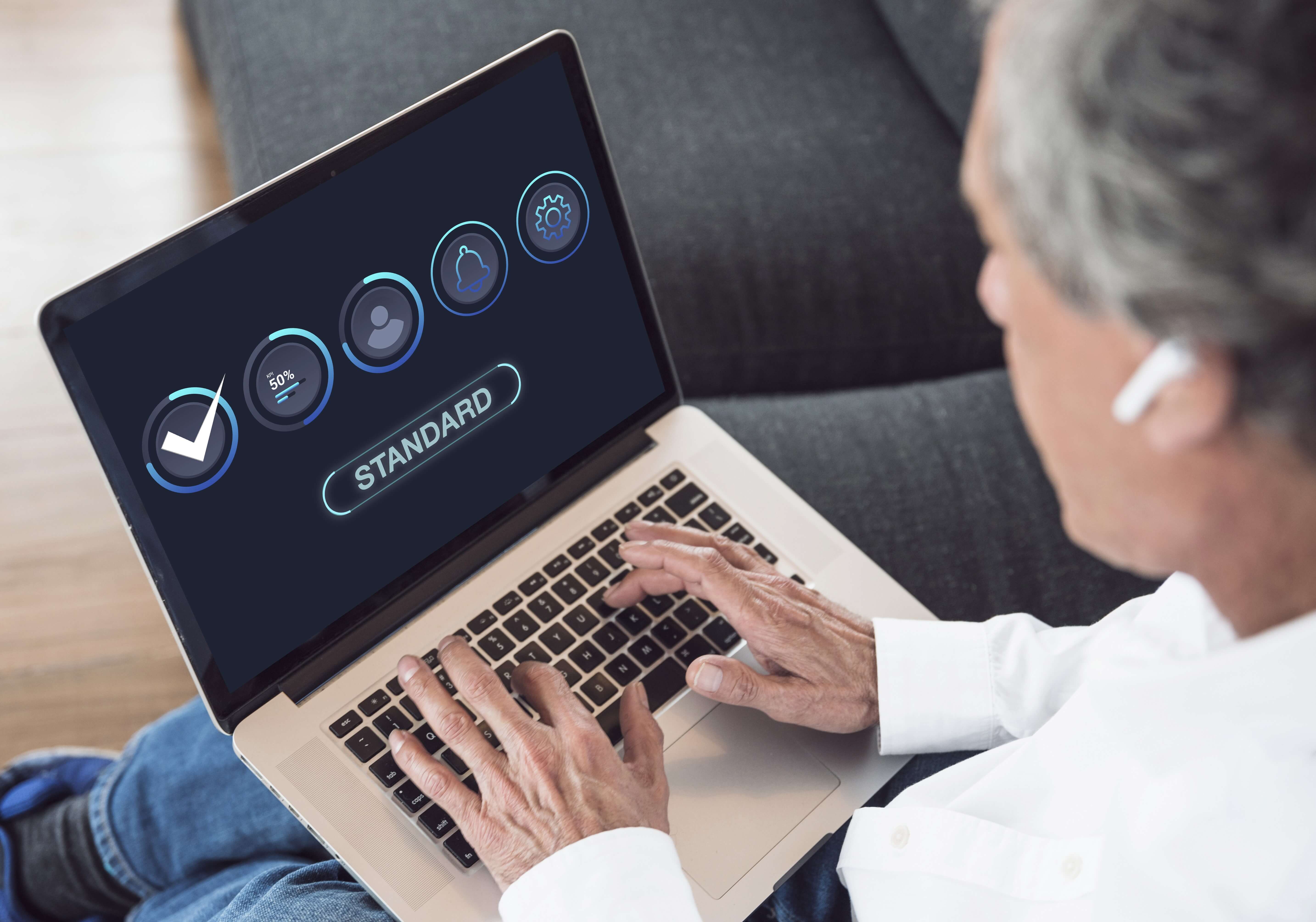 Over-the-shoulder view of a person using a laptop displaying a quality assurance dashboard with "STANDARD" text and various status icons.
