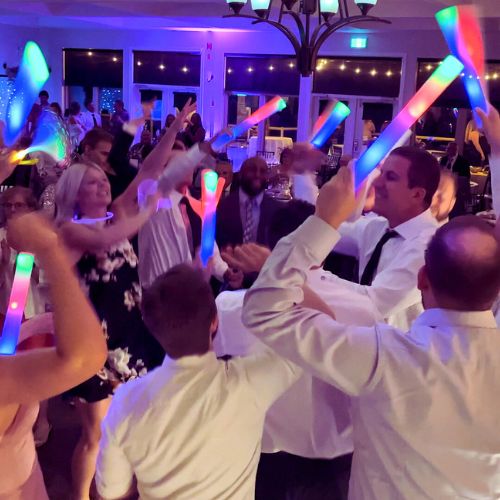 A joyful couple sharing a dance at their wedding reception, surrounded by guests in a beautifully lit banquet room with colorful lights creating a festive atmosphere.