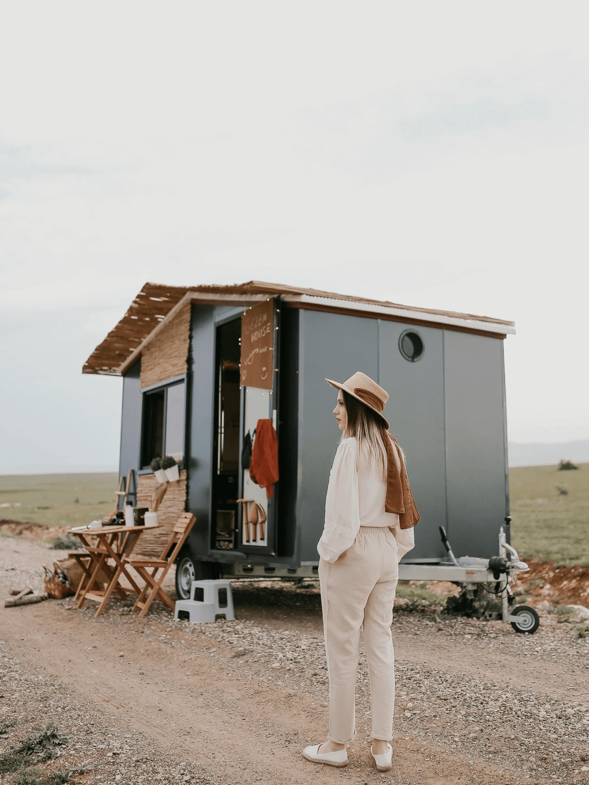 Frau steht vor einem Tiny House und schaut in die Ferne