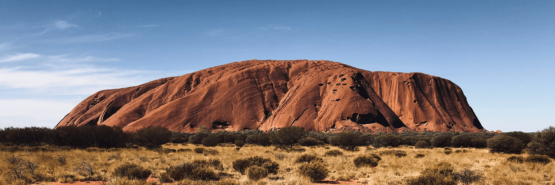 Uluru rising from the red desert landscape under a clear blue sky, Northern Territory