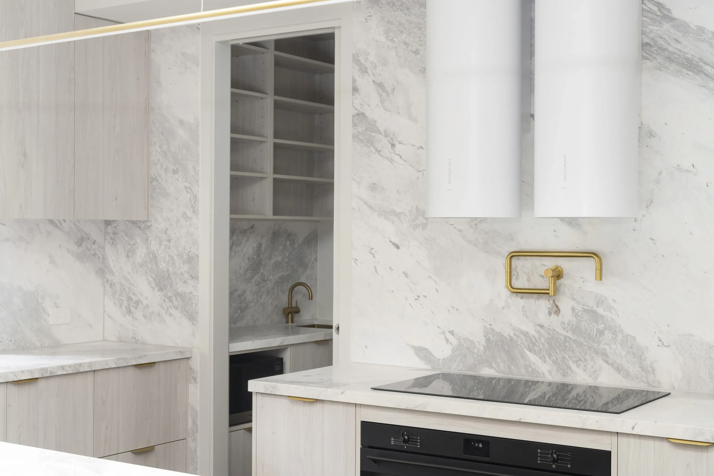 Close-up of the Bundoora kitchen induction cooktop with brass pot filler against full-height marble, butler’s pantry visible beyond