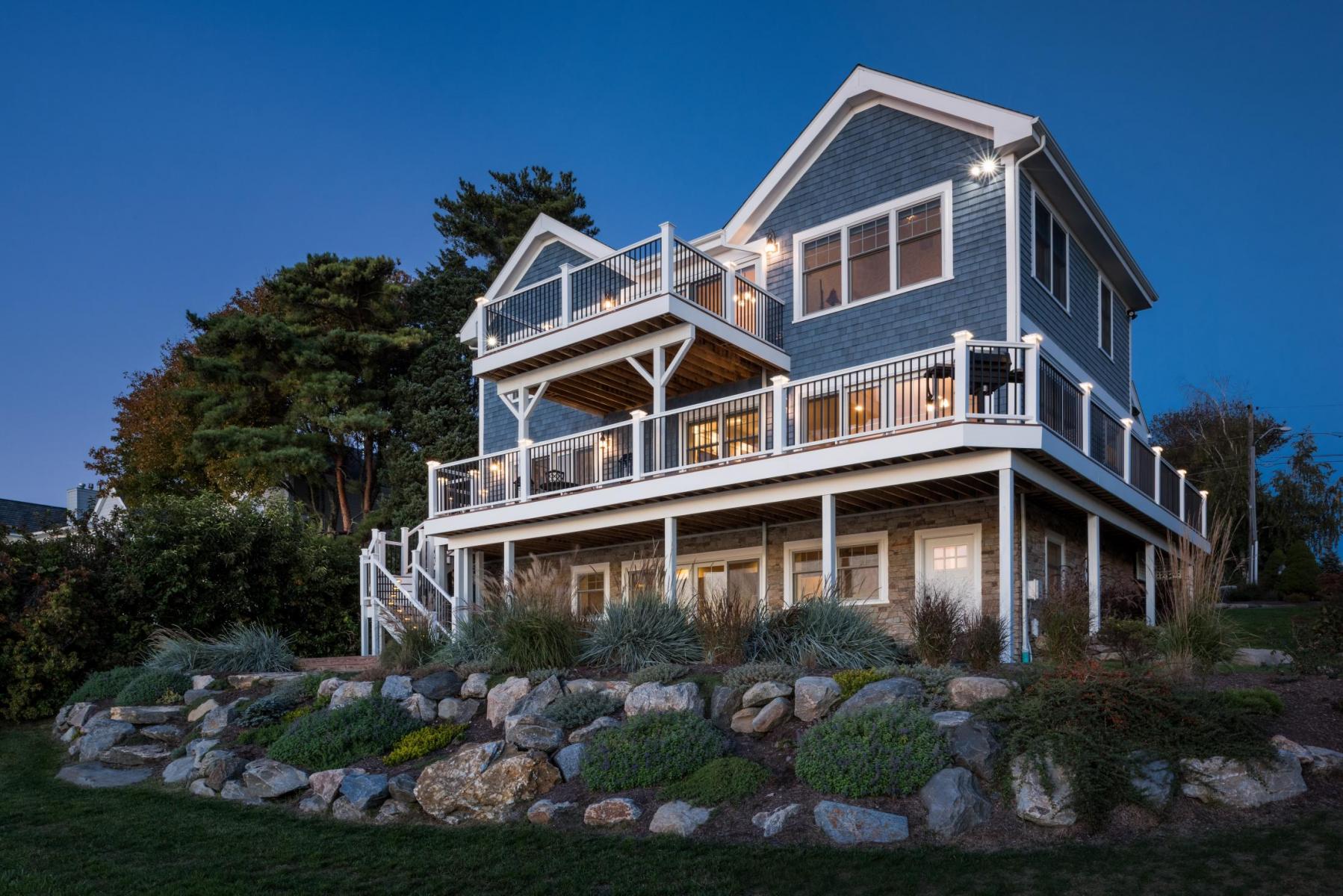 A large, multi-story house with a wraparound porch, set against a twilight sky and surrounded by greenery.