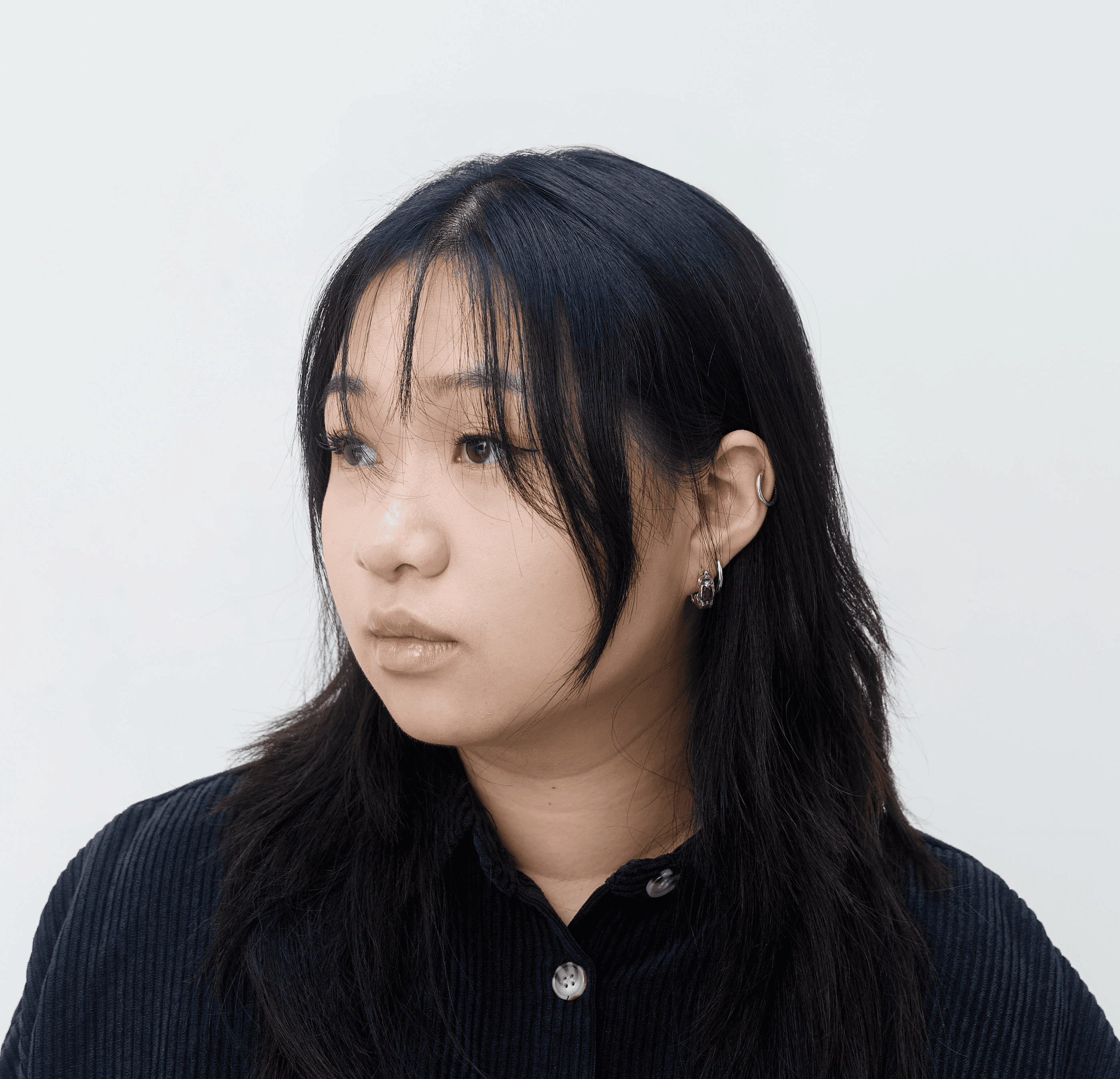 A person with curly hair and glasses smiles at the camera, seated in a cozy workspace with warm lighting.