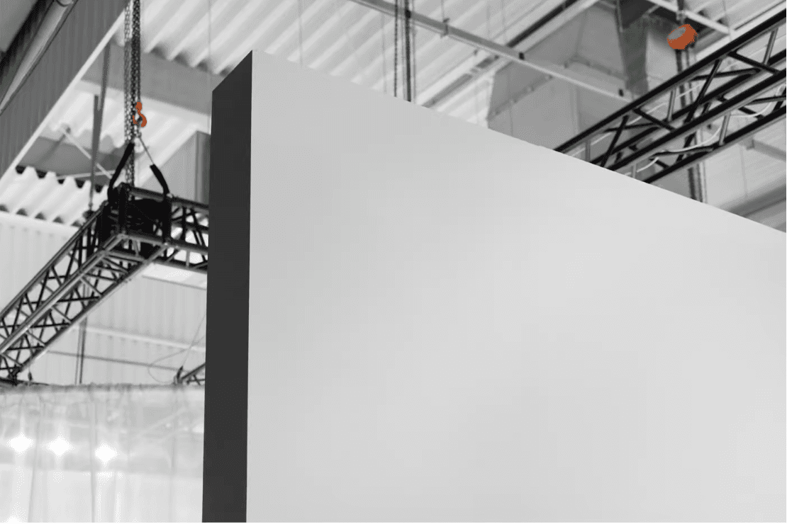 Mockup of a large green wall panel in an industrial exhibition setting. Overhead trusses and ceiling structures frame the space, providing a professional backdrop for branding or event signage.