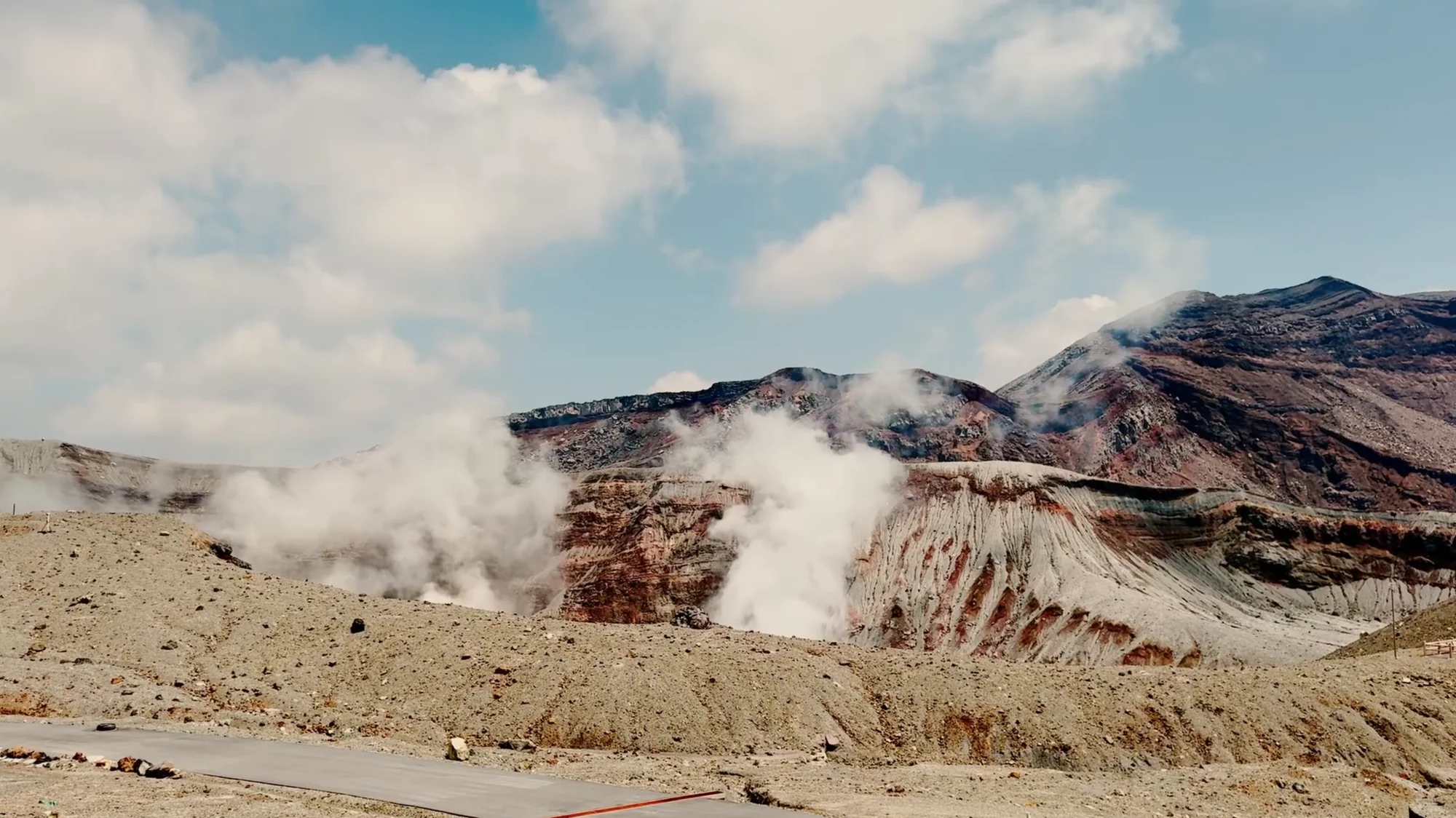 Steam venting white from the bare flank of a volcanic ridge under blue sky