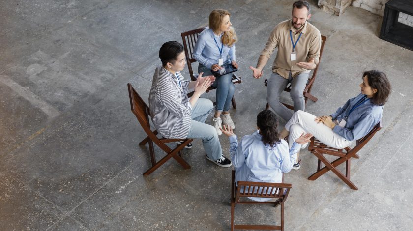 Five people in a circle sitting on chairs and talking to eachother