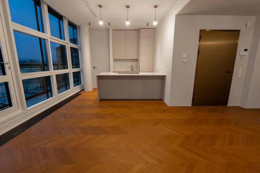 Moderner Wohnbereich mit Küchenzeile, großer Fensterfront und hochwertigem Chevron-Parkettboden.