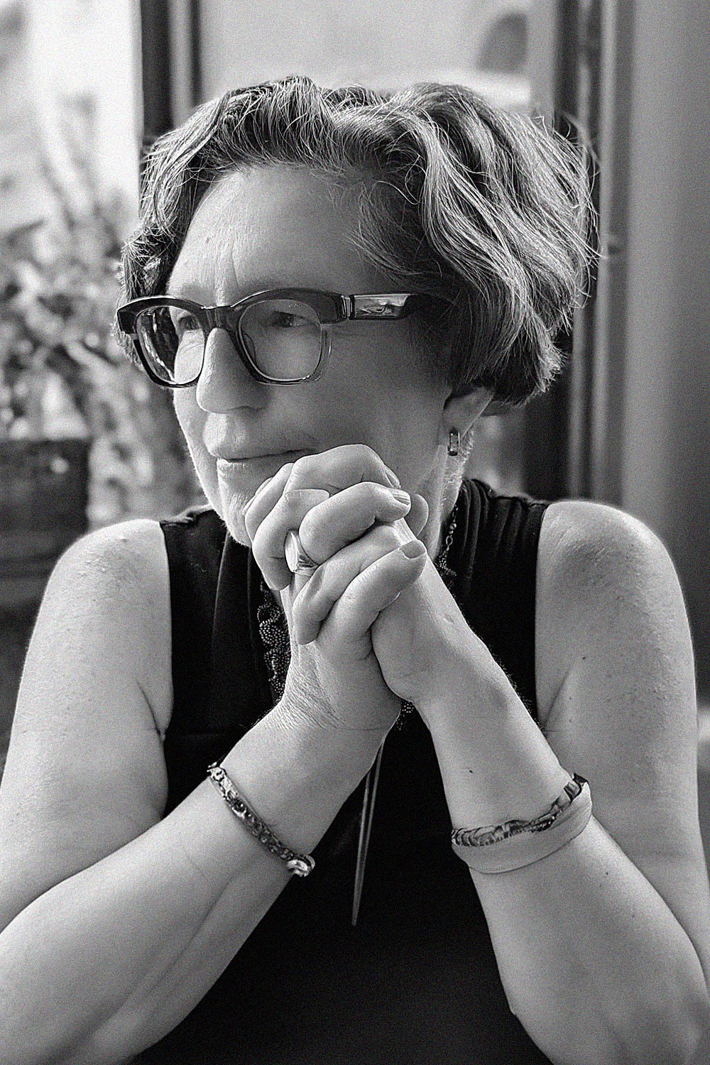 A young woman with long dark hair smiles confidently while crossing her arms in a modern indoor setting.