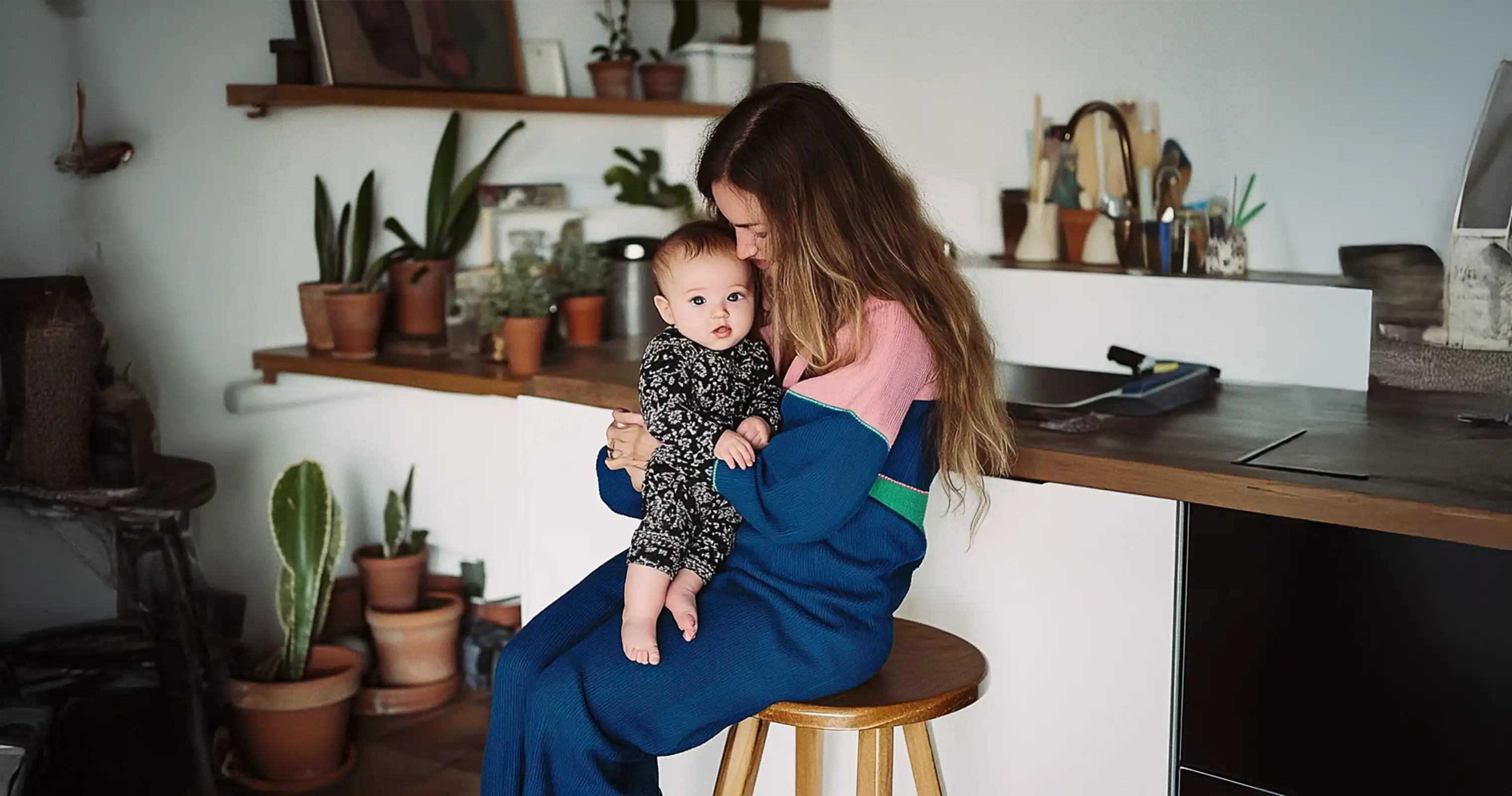 A caring nanny holding a baby in a cozy kitchen, representing the flexibility and 24/7 support provided by ROTA nannies.