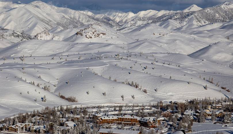Scenic winter landscape with snow-covered mountains, rolling hills, and a small town at the base of the mountains.
