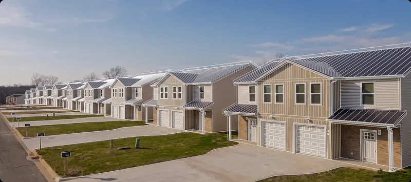 Brushwood Duplex: a long row of tan and grey two-story duplex homes with dark metal roofs, awnings and paired garages along a shared driveway