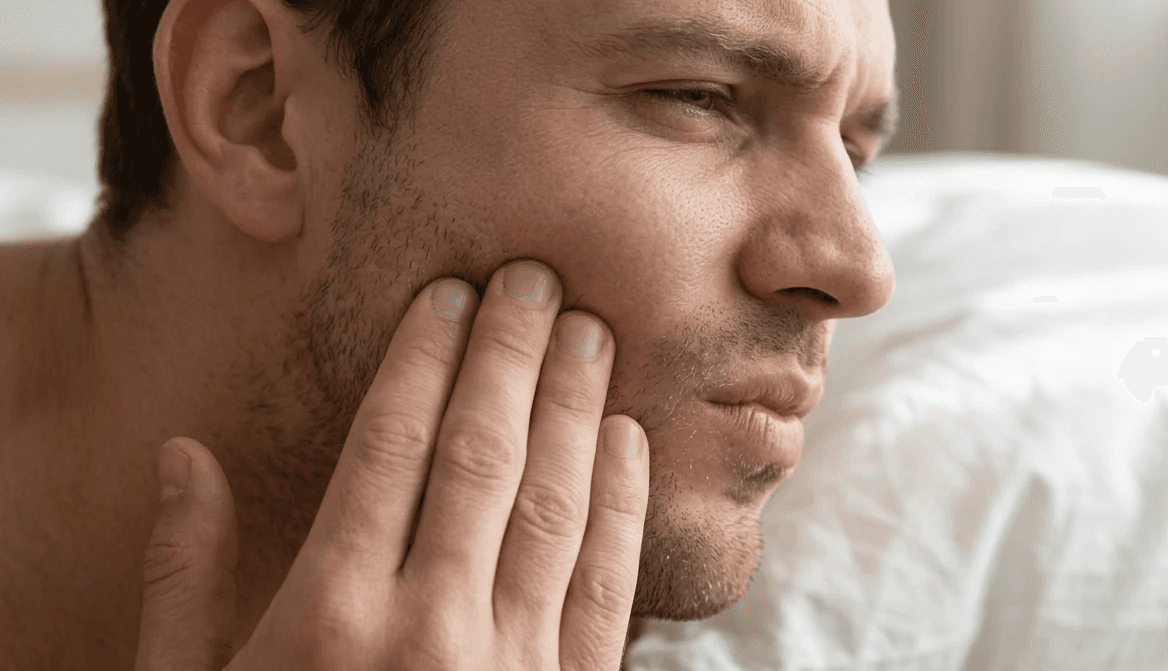 رجل يمسك خده بسبب تشنج عضلات الفك عند الاستيقاظ، وهو عرض شائع ناتج عن صرير الأسنان أثناء النوم