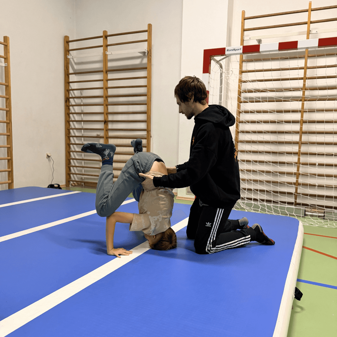 Trenerzy Nikola i Tobiasz asekurujący uczennicę do salta w tył na zajęciach z akrobatyki w Rabce Zdrój