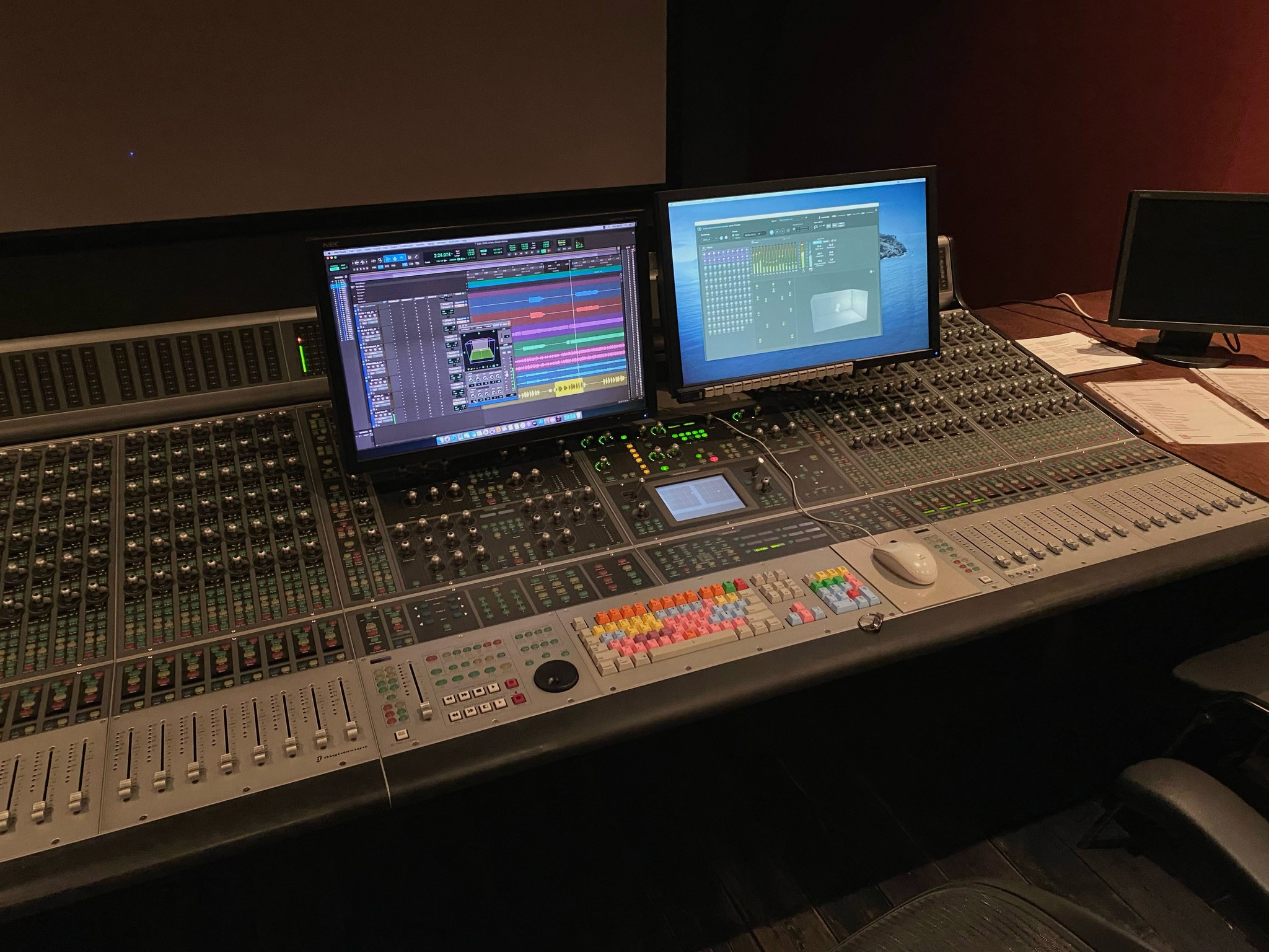 Professional mixing console and Dolby Atmos studio setup featuring dual monitors displaying a digital audio workstation (DAW) interface and surround sound panning tools, highlighting a state-of-the-art environment for precise music mixing and mastering.