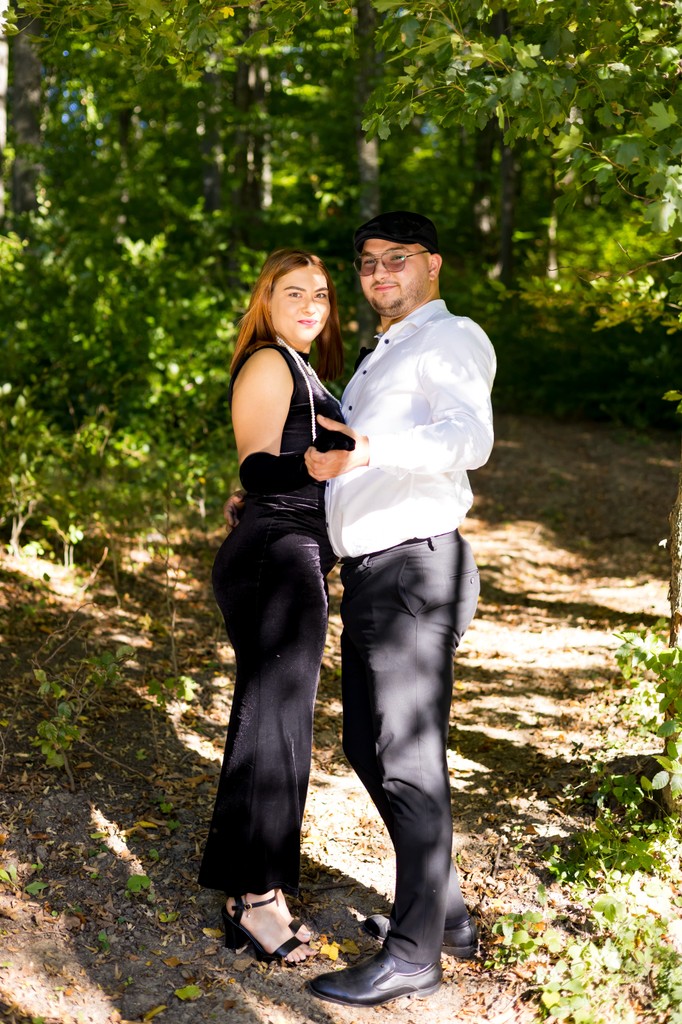 A smiling couple sits on a white blanket in a lush green field.