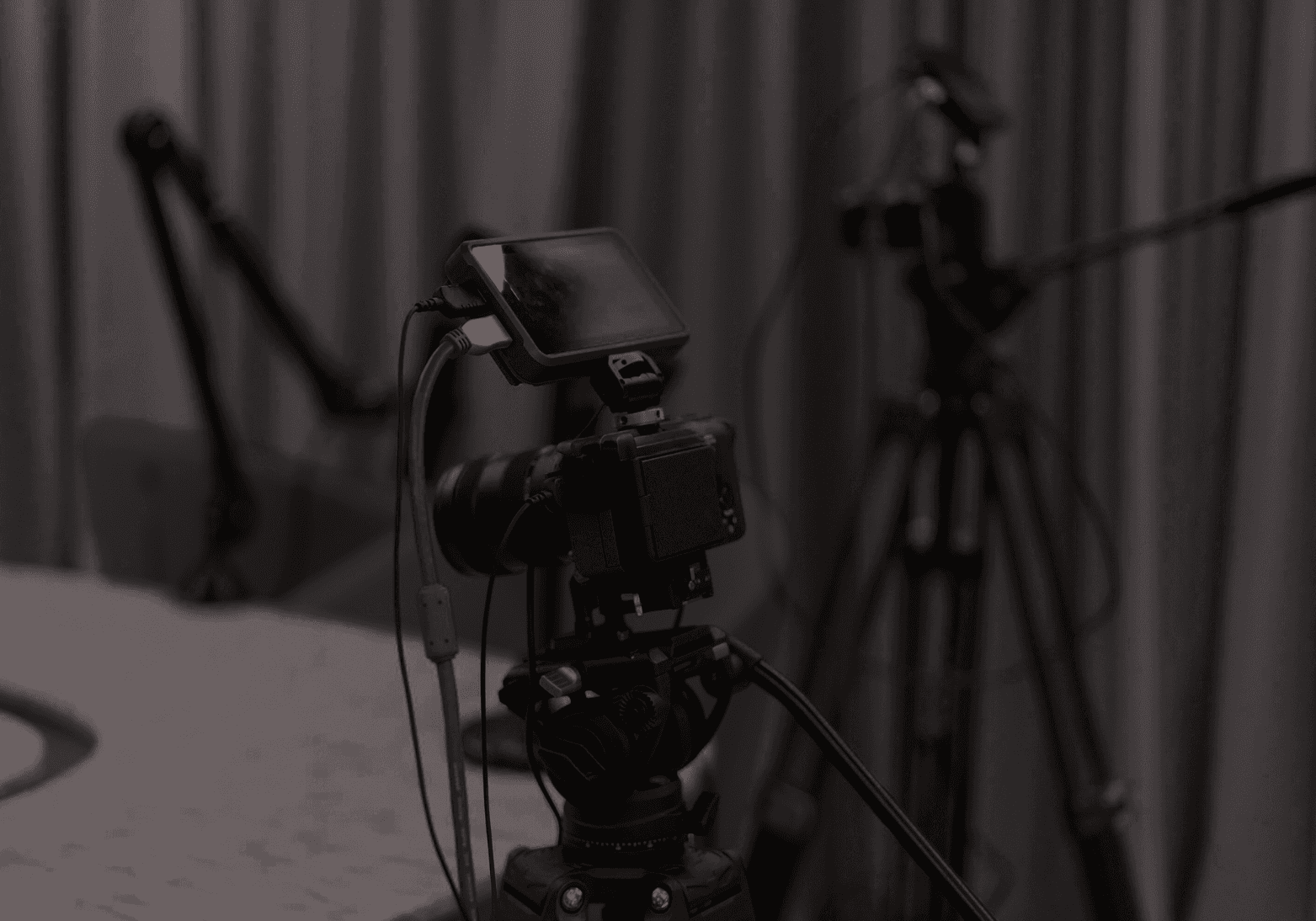 A person working on their home office desk with their headphones on. The lighting is dark with subtle,soft lights coming from a lamp