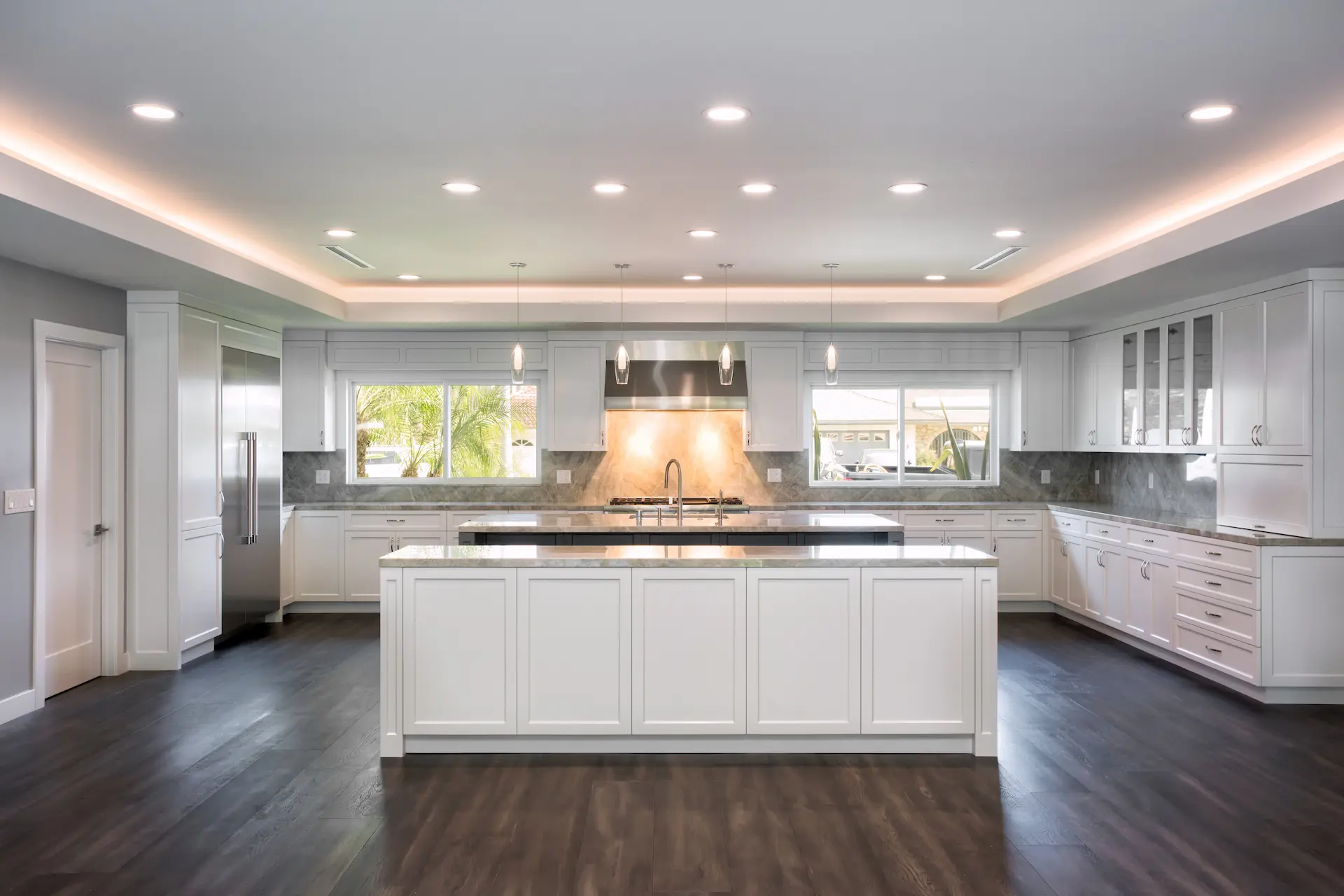 Spacious kitchen with white cabinetry, central island, hardwood floors, and pendant lighting in Costa Mesa Remodel. Photo by Chris Darnall.