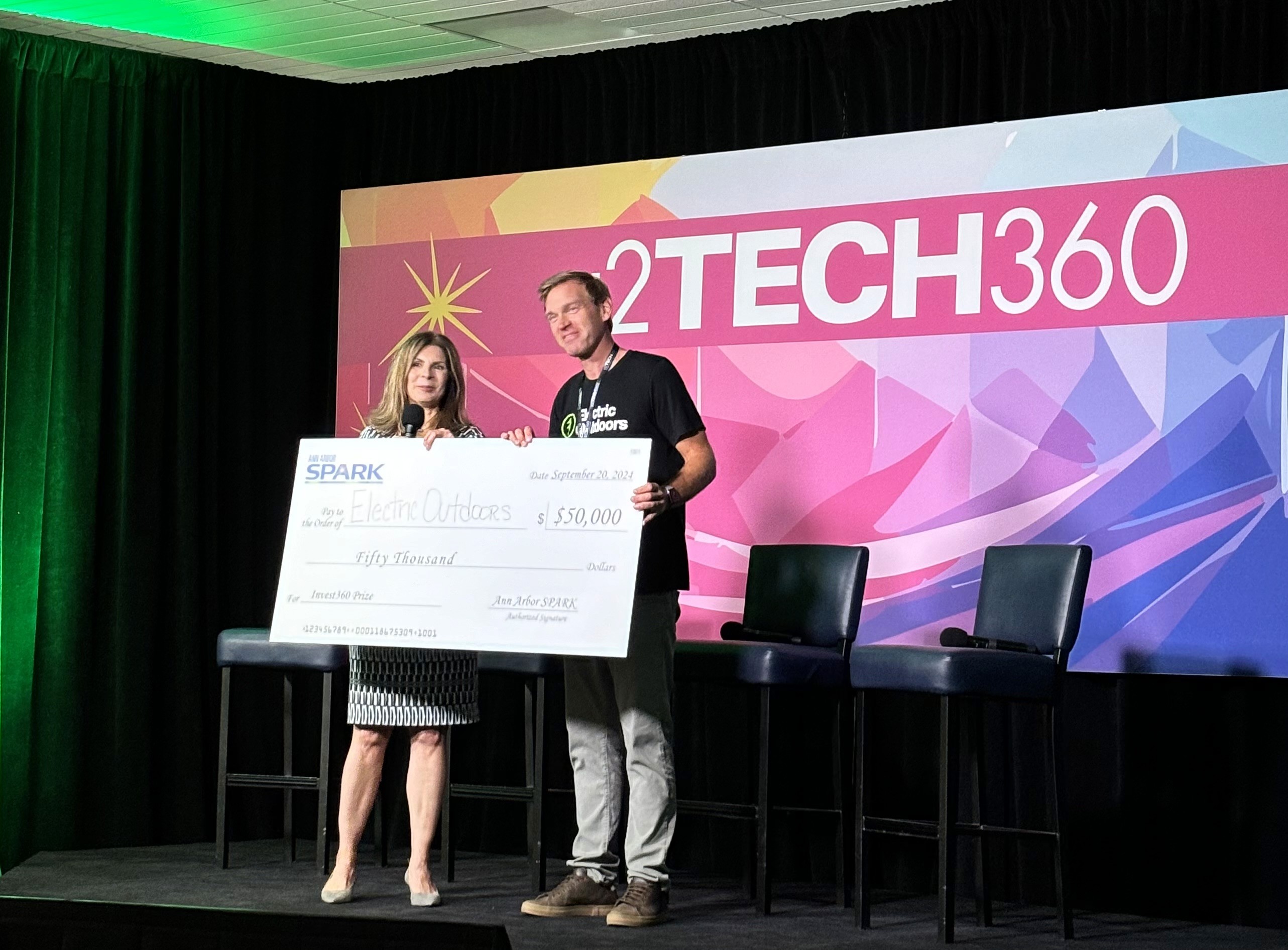 Two people on stage holding a large check for $50k