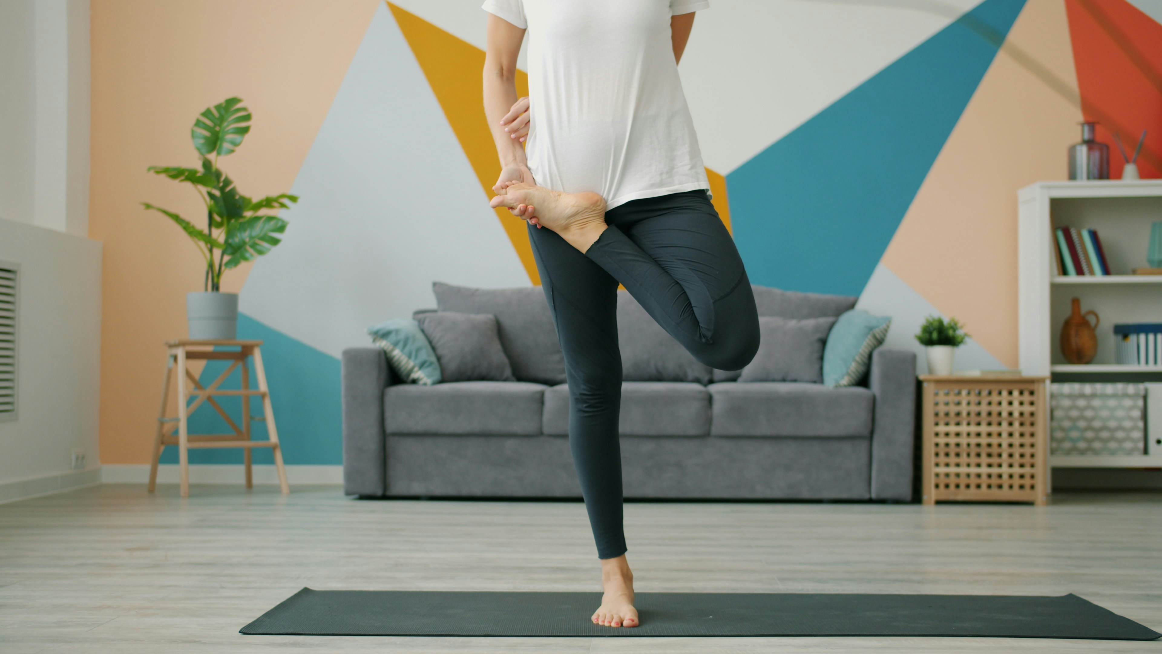 Woman practicing yoga tree pose on mat indoors.