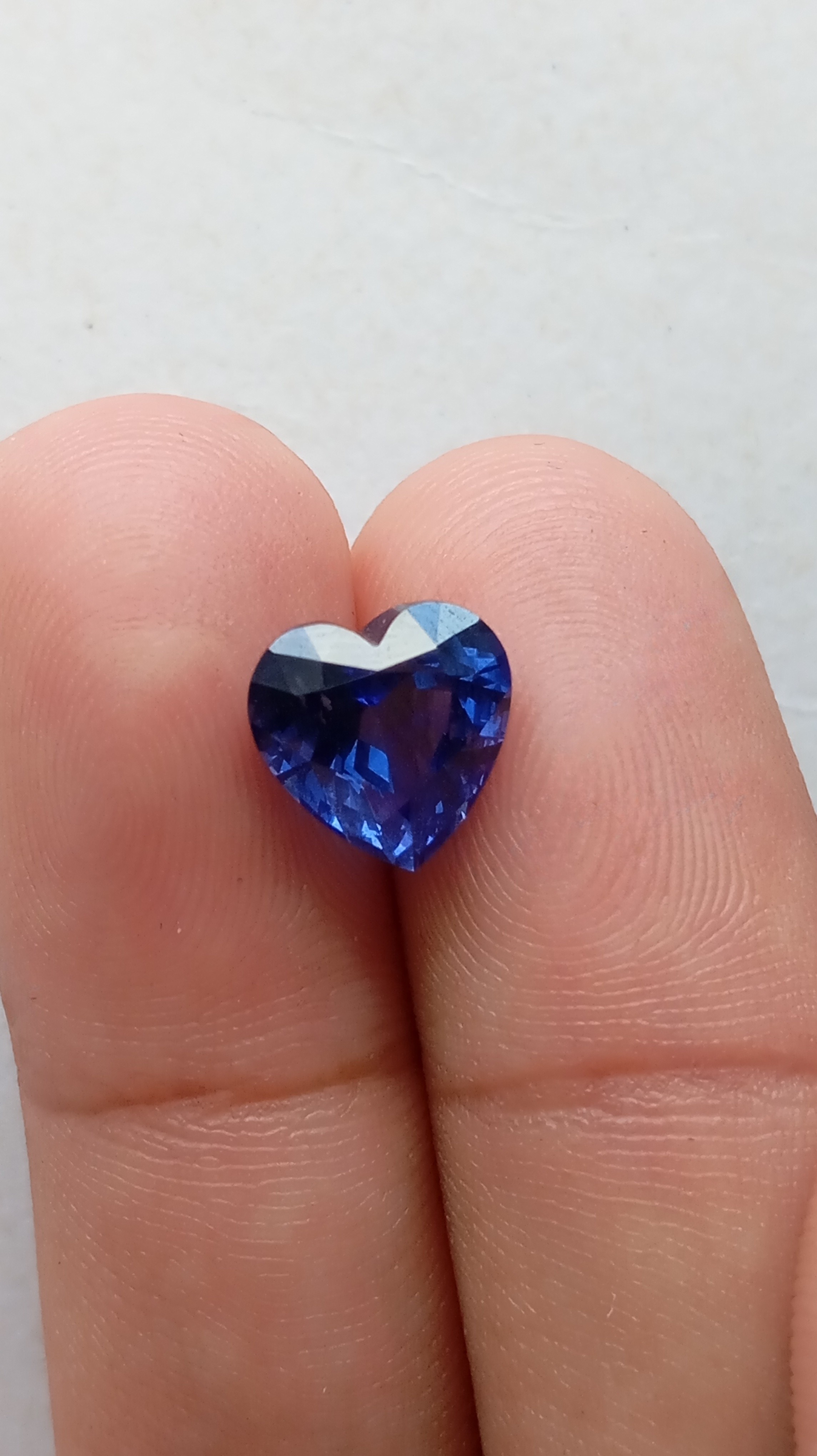 Macro closeup showing the facet patterns and clarity of a blue lab-grown sapphire in fingers.