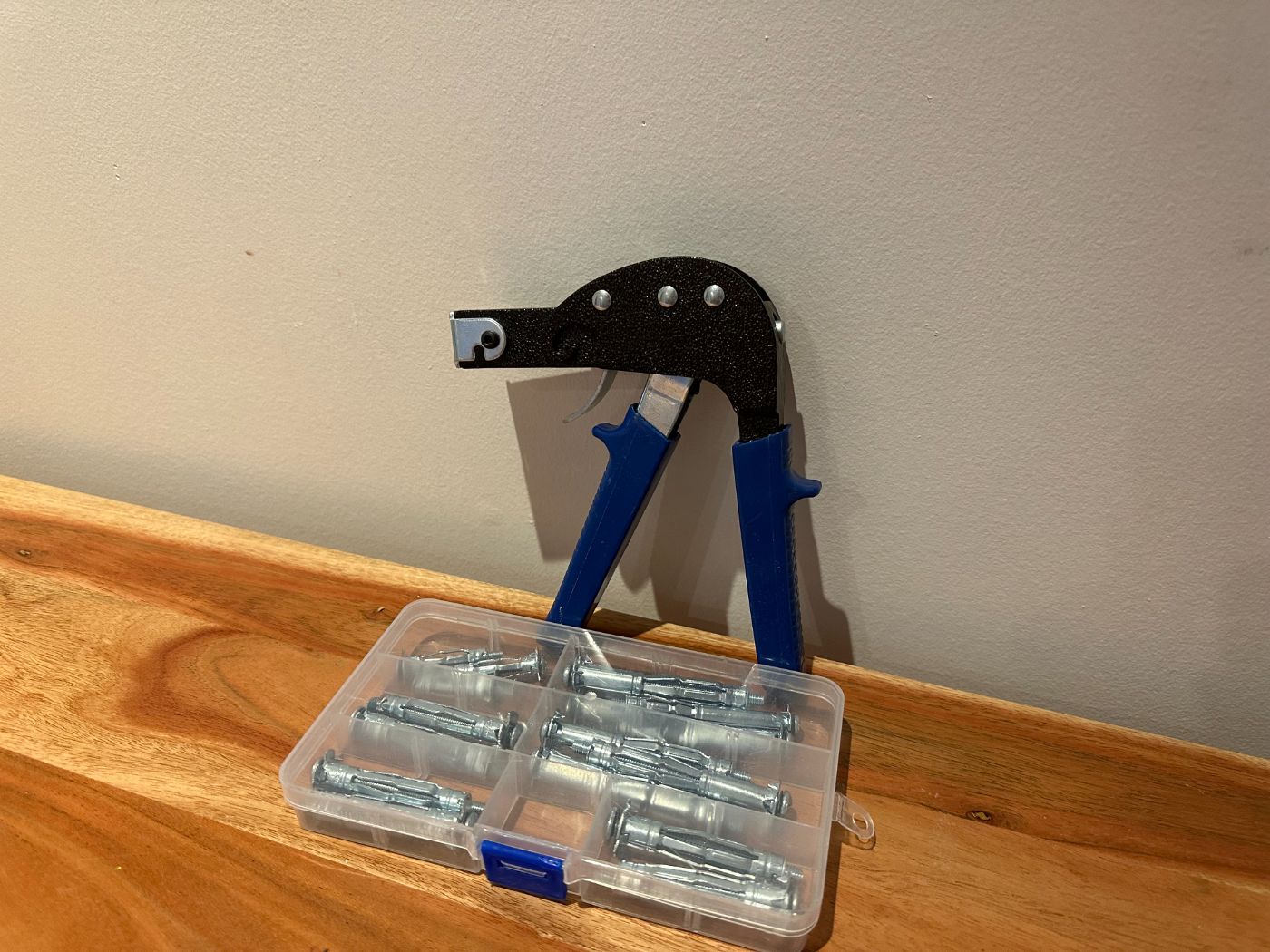 Pince à cheville avec assortiment de chevilles métalliques pour cloison sèche dans une boîte en plastique, posées sur une table en bois