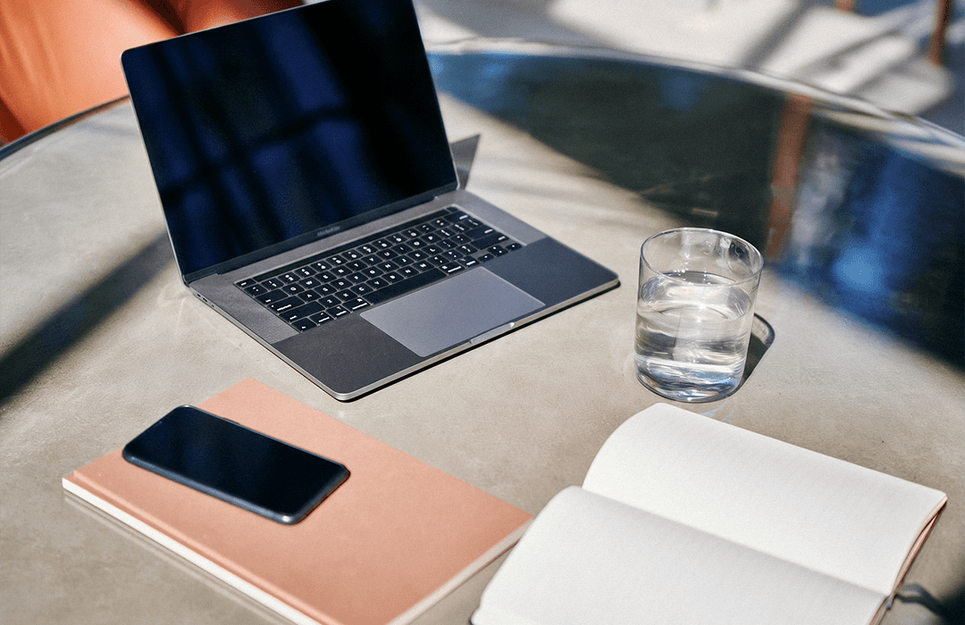 MacBook, celular e caderno organizados sobre mesa de vidro em ambiente de trabalho. Blog post Inspira.